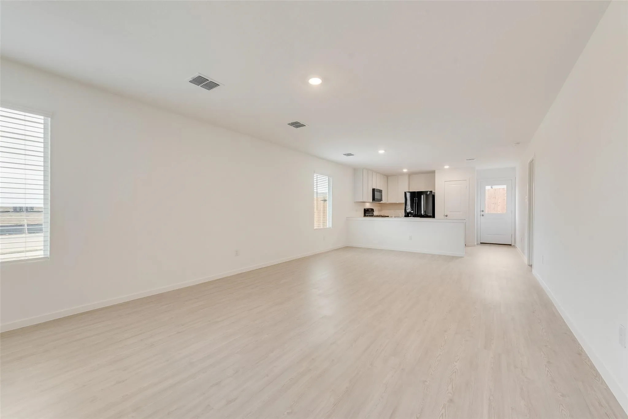 Open-concept living space with light wood-finish flooring, recessed lighting, and a kitchen featuring white cabinetry and black appliances