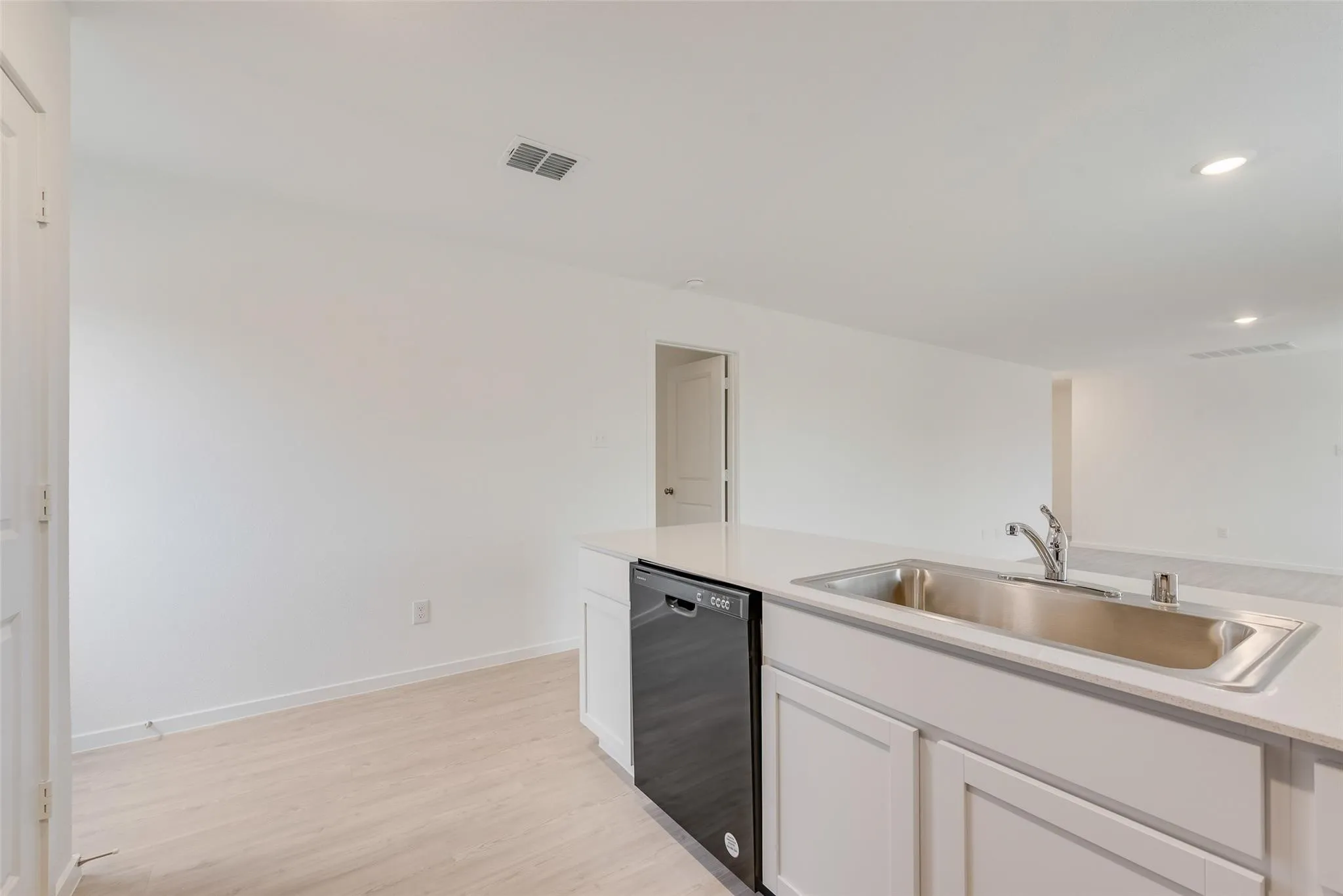Kitchen island featuring a stainless steel sink, chrome faucet, integrated dishwasher, and white cabinetry with a light-colored countertop