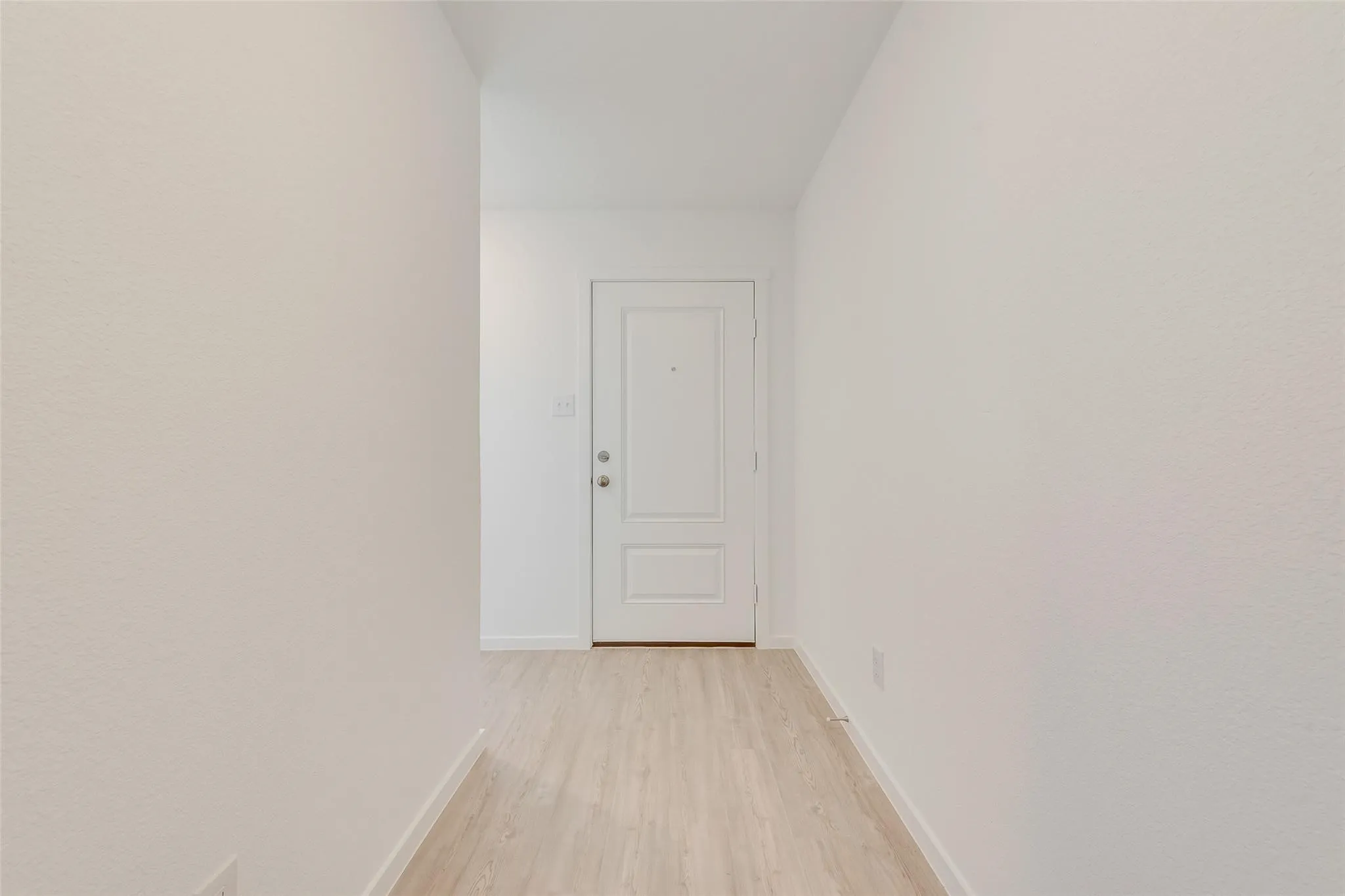 Wood-finish flooring with white walls and a paneled entry door