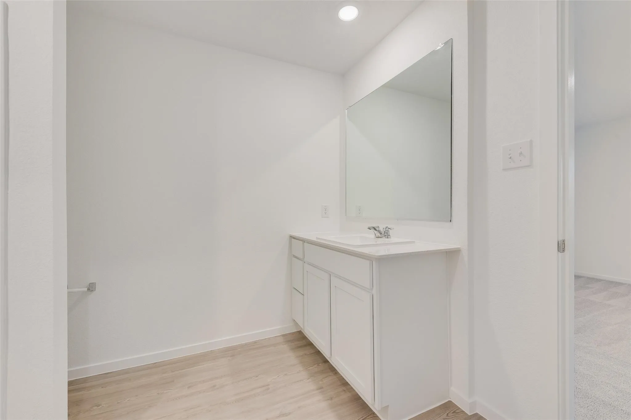 Single vanity with white cabinetry, integrated sink, and wall-mounted mirror