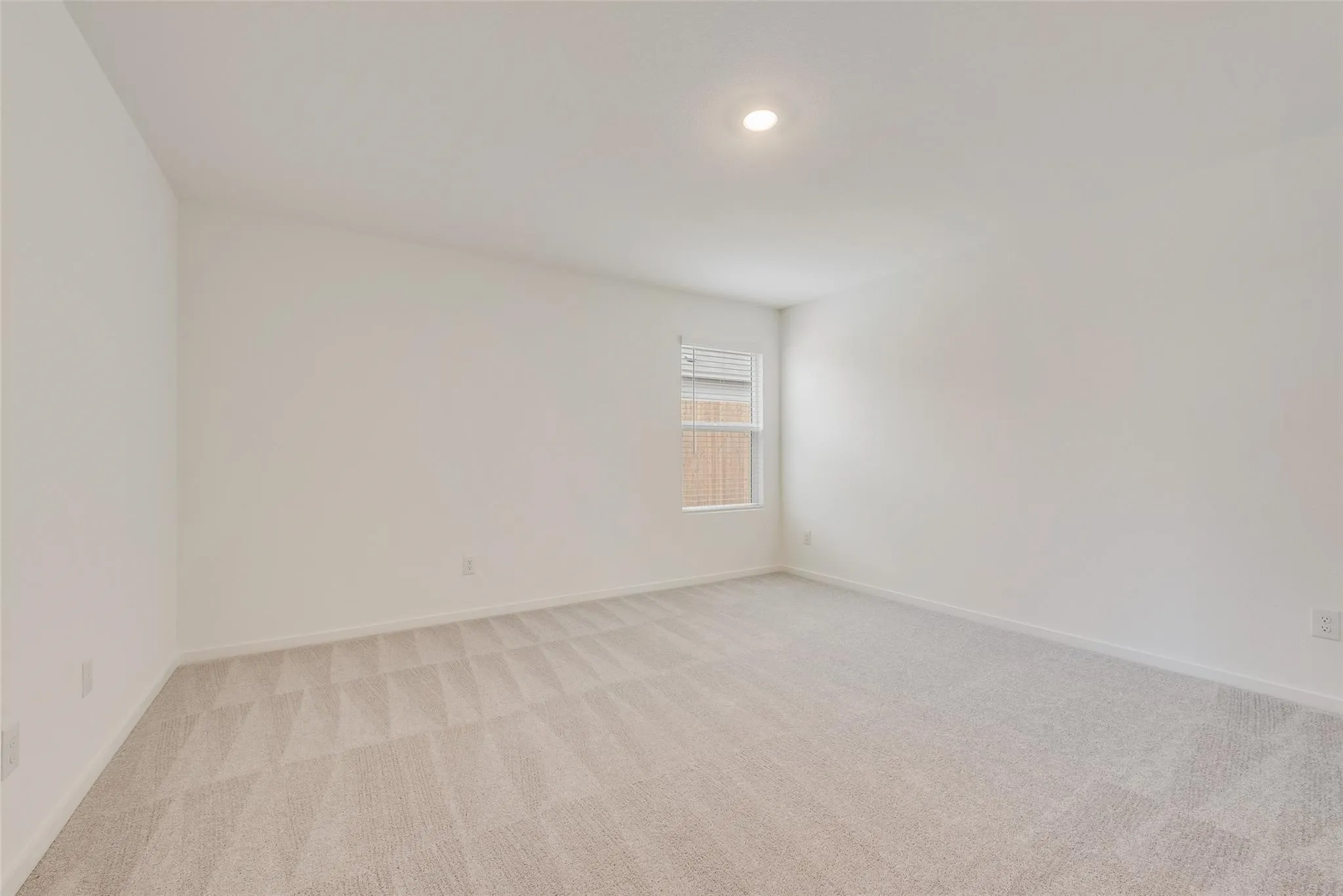 Recessed ceiling light, neutral wall paint, window with blinds, and patterned carpeting