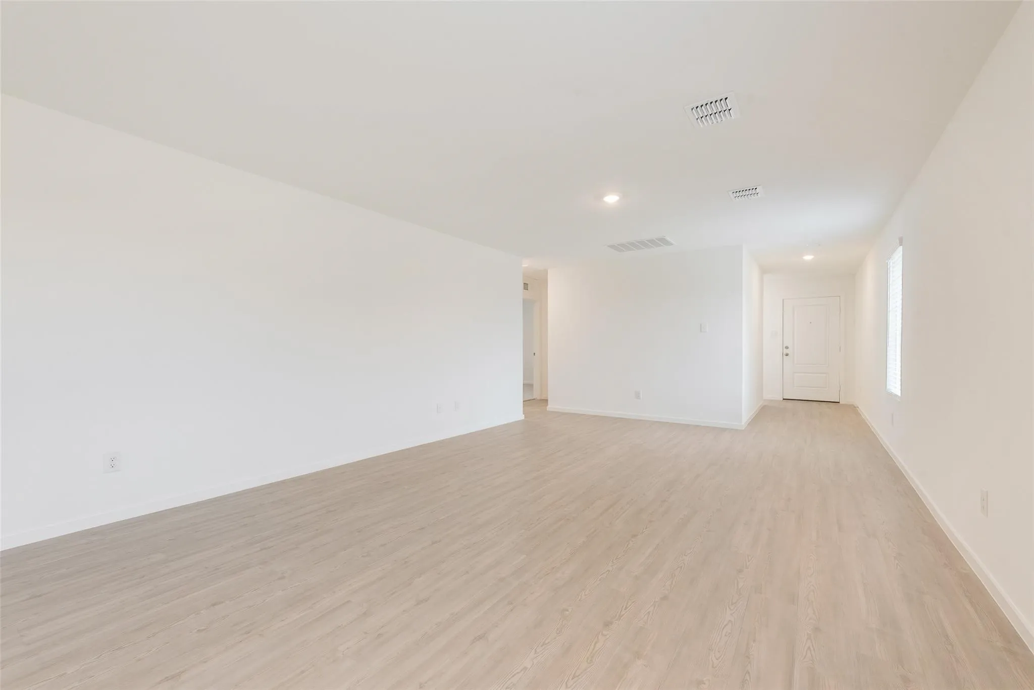 Spacious room featuring light wood-finish flooring, recessed lighting, and a white paneled door