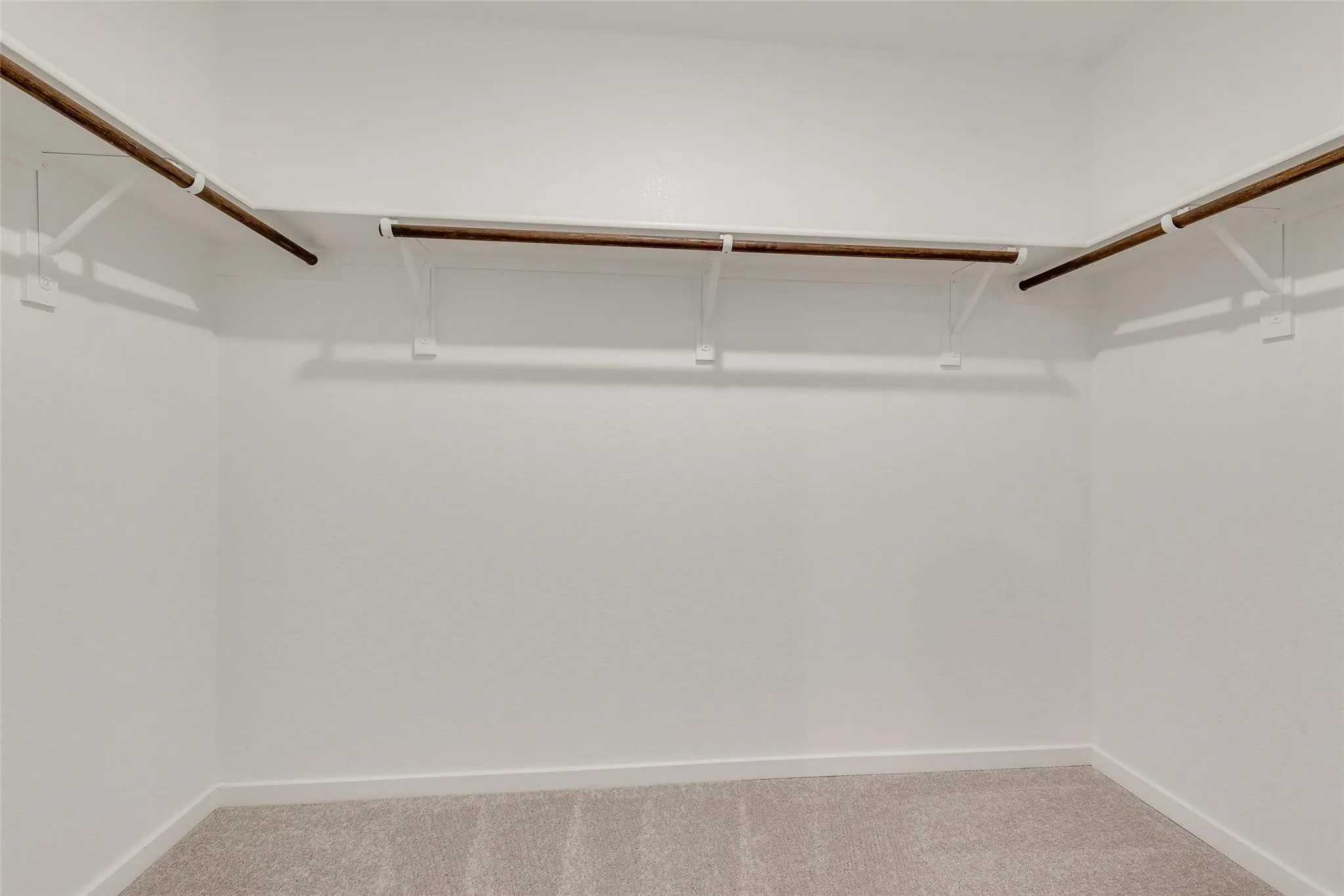 Walk-in closet featuring light gray carpet flooring, white walls, and built-in wood-finish shelving and hanging rods