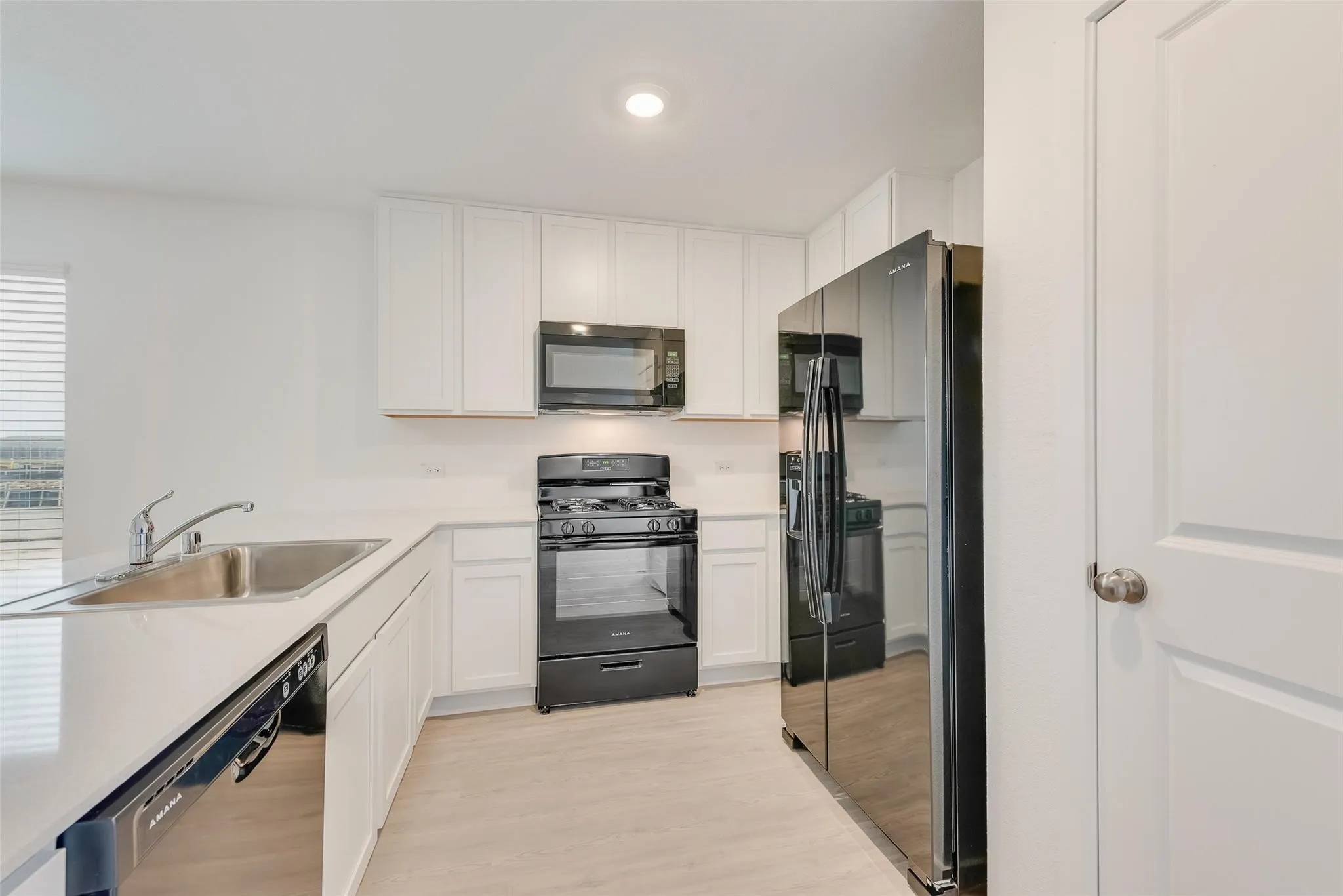Kitchen with white cabinetry, stainless steel sink, and black appliances