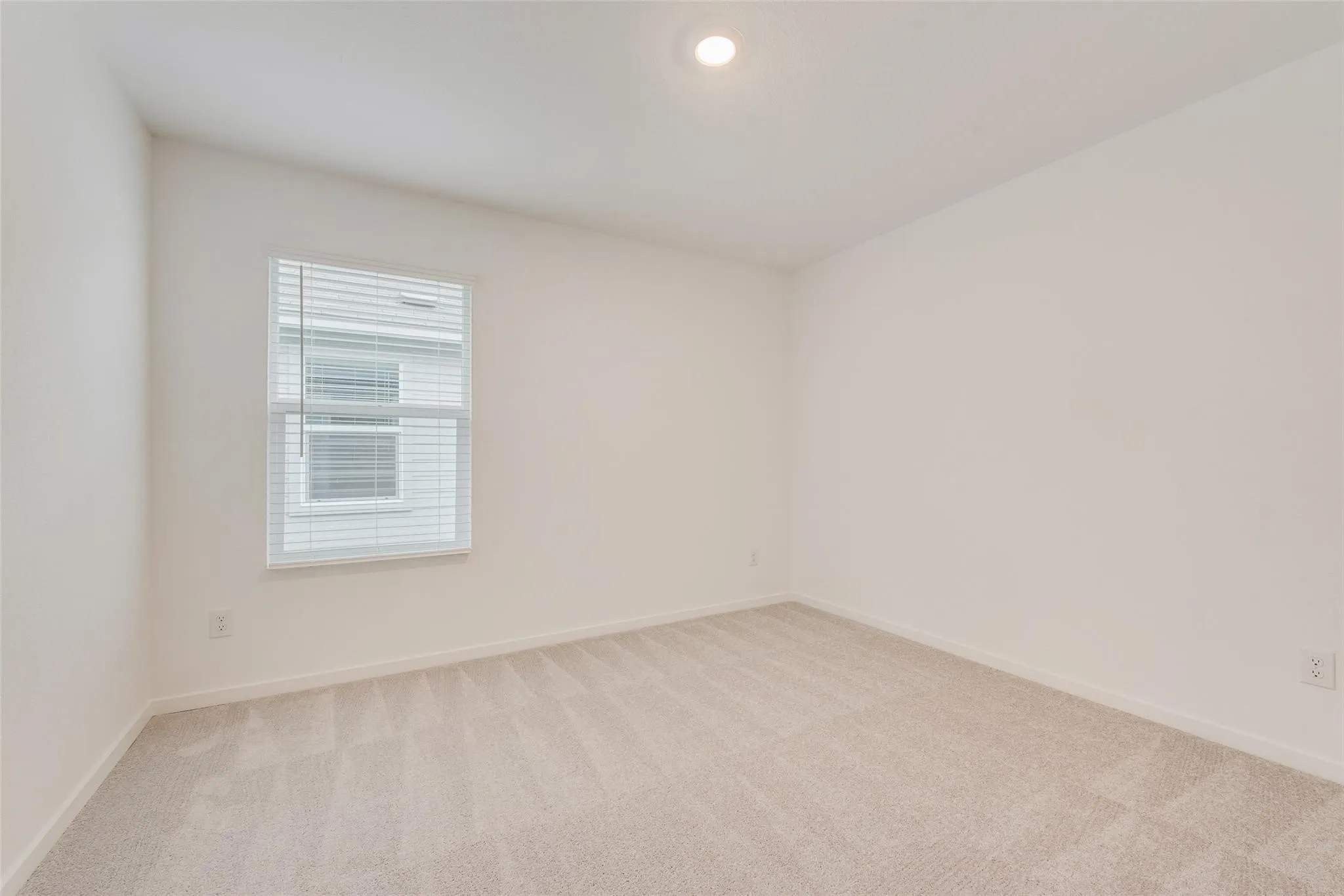 Recessed ceiling light, neutral wall color, window with blinds, and light-toned carpeting