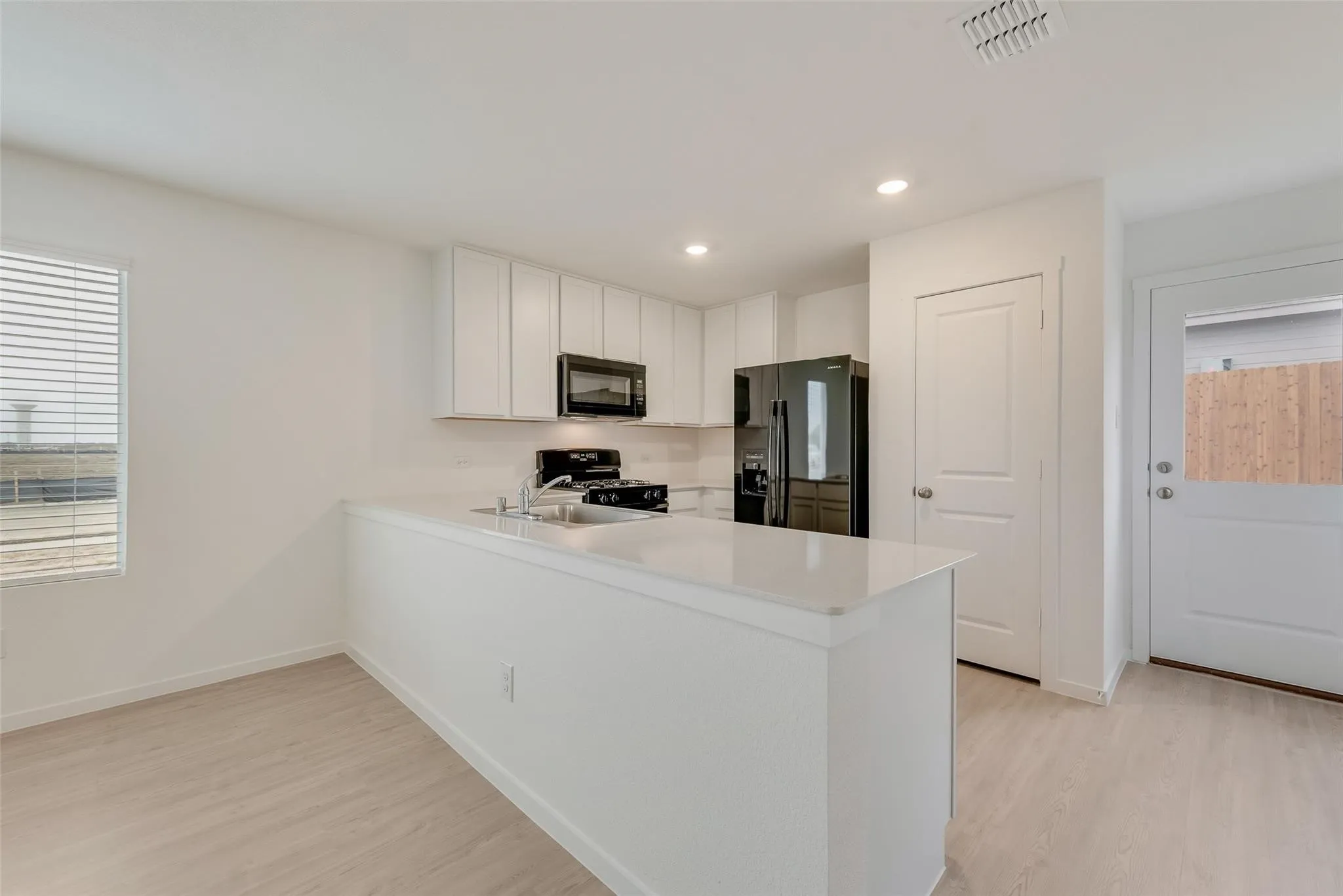 Kitchen featuring white upper and lower cabinetry, stainless steel sink, black appliances, and light wood-finish flooring