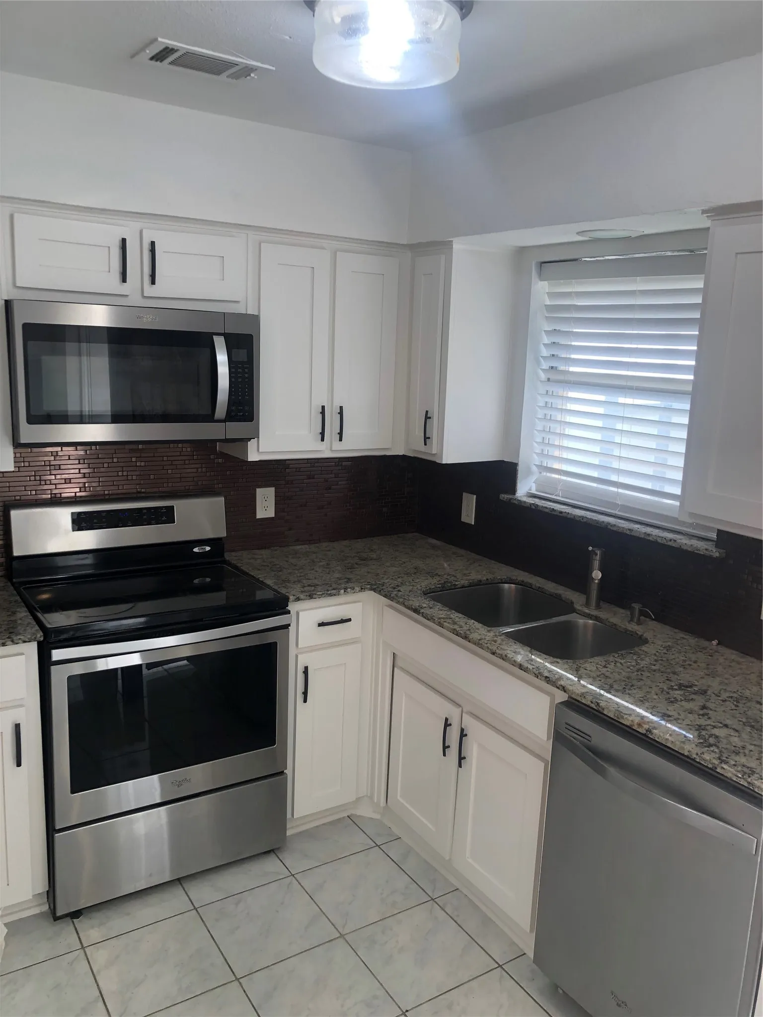 White cabinetry, stainless steel appliances, mosaic tile backsplash, granite-finish countertops, and square tile flooring