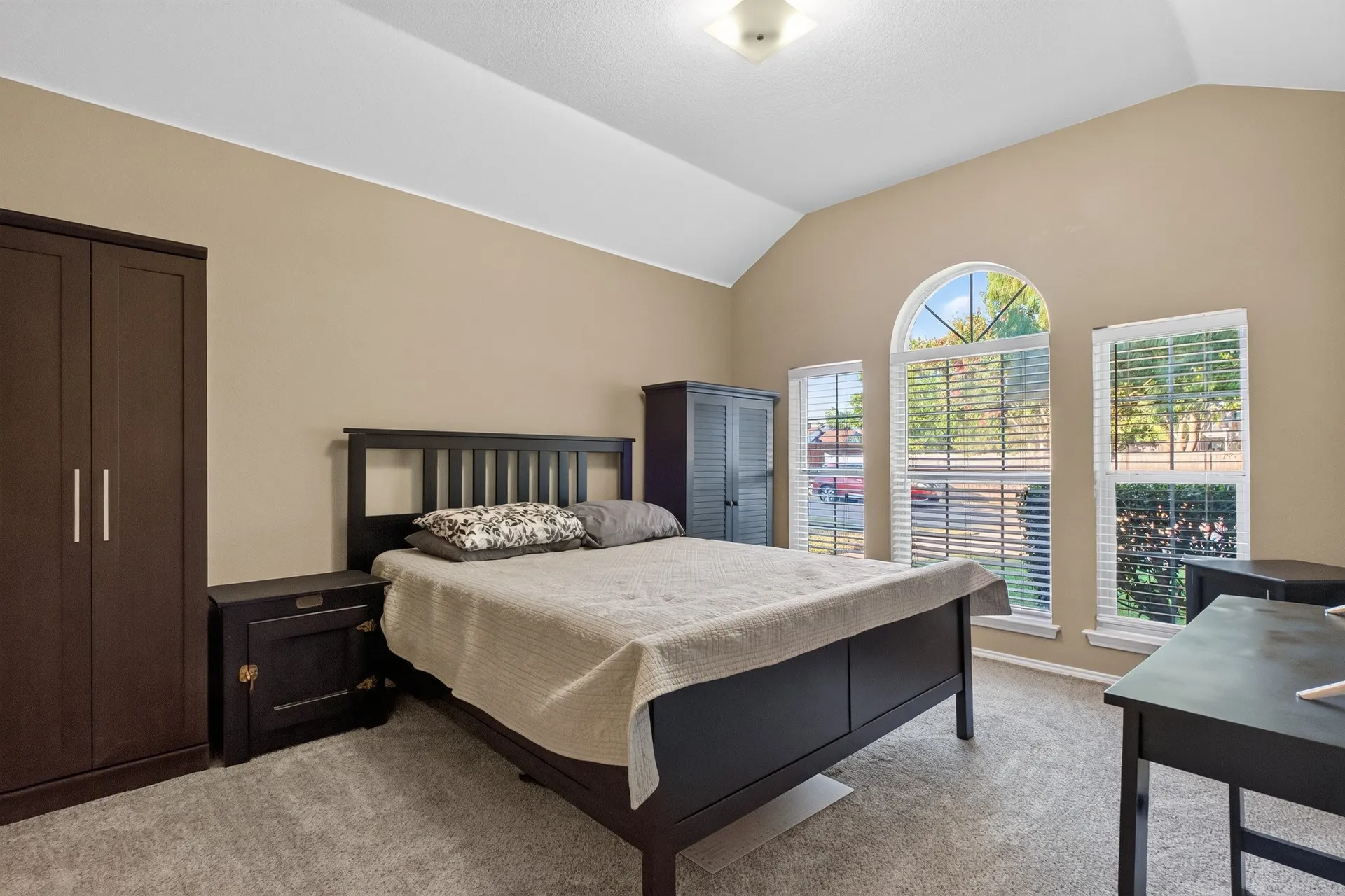 Vaulted ceiling with an overhead light fixture, carpeted flooring, and a large arched window with side windows