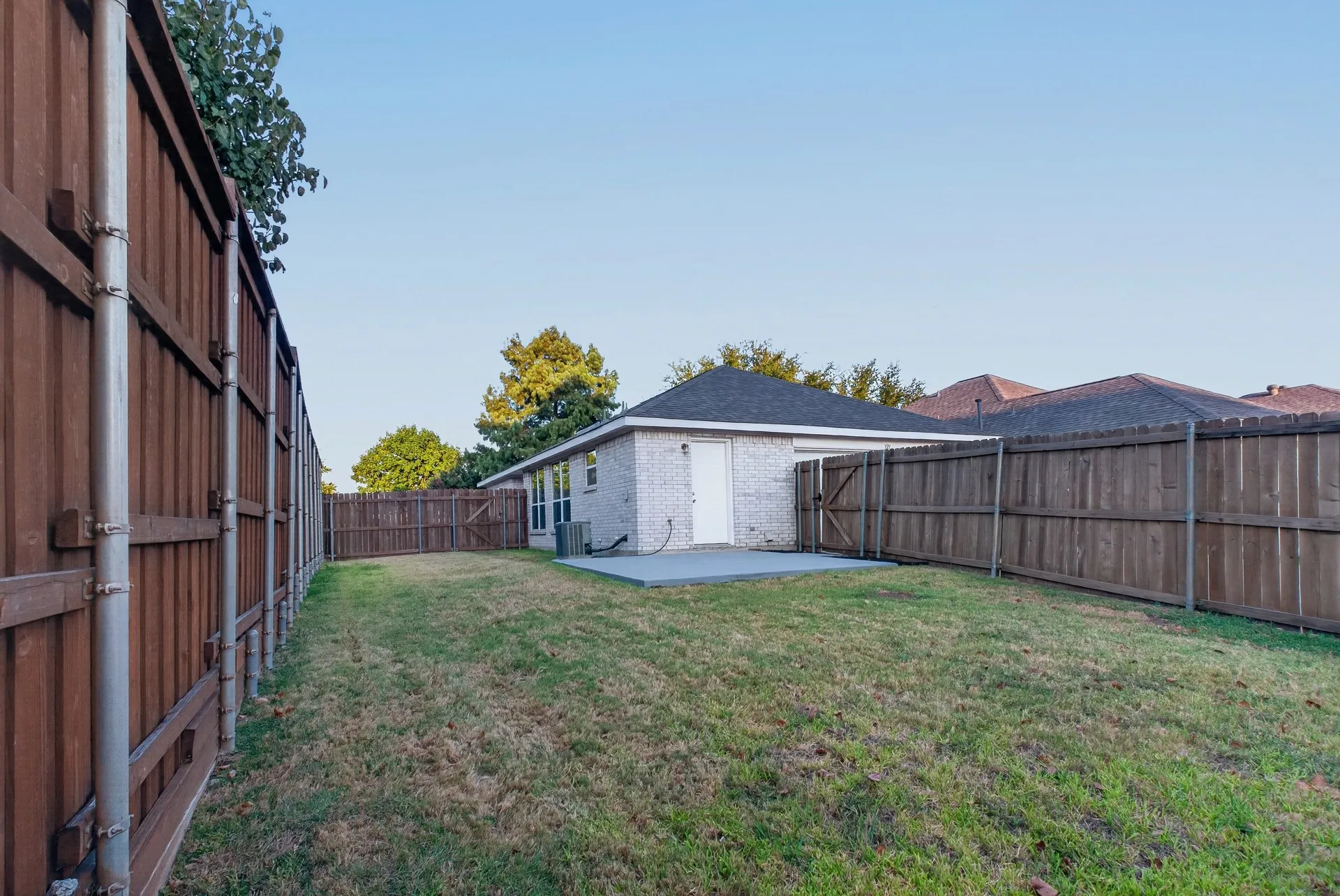 Expansive fenced backyard with a concrete patio, brick exterior, and a dark shingle roof
