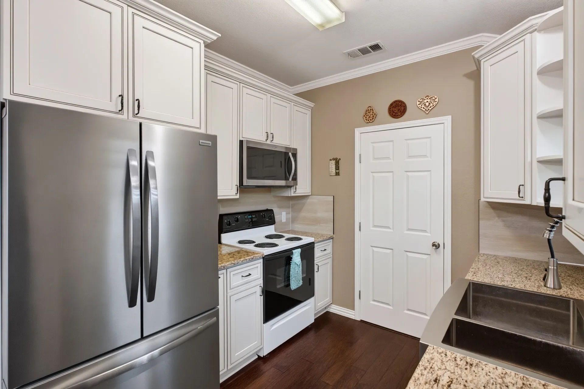 White cabinetry with crown molding, stainless steel refrigerator, built-in microwave, dark wood-finish flooring, and granite countertops