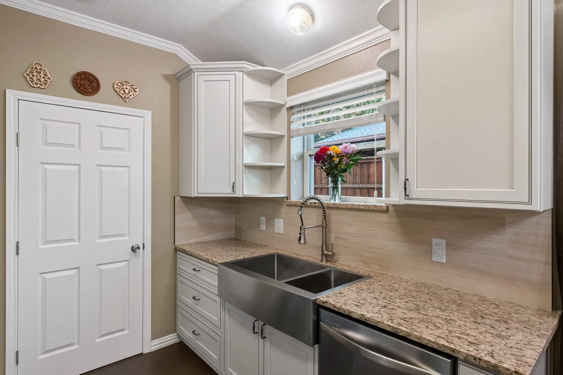 Stainless steel farmhouse-style sink with a gooseneck faucet, light-toned countertops, tile backsplash, and white cabinetry