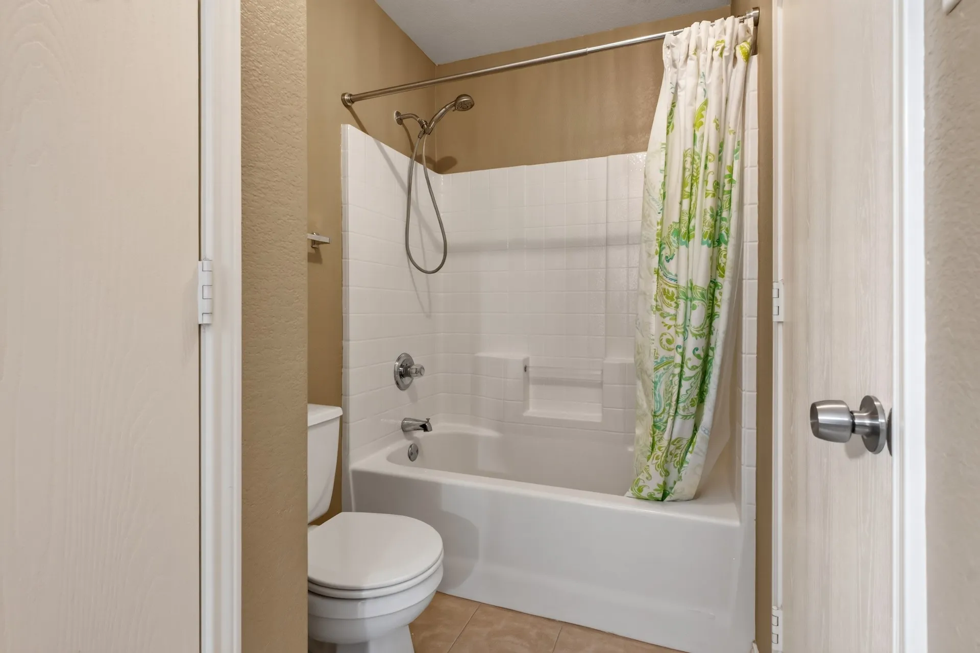 Built-in tub with white tile surround, chrome shower fixtures, and a white toilet