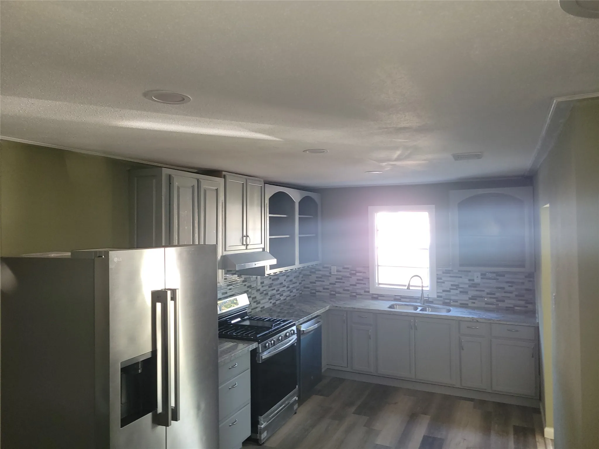 Light-toned cabinetry, stainless steel appliances, mosaic tile backsplash, wood-finish flooring, and recessed lighting
