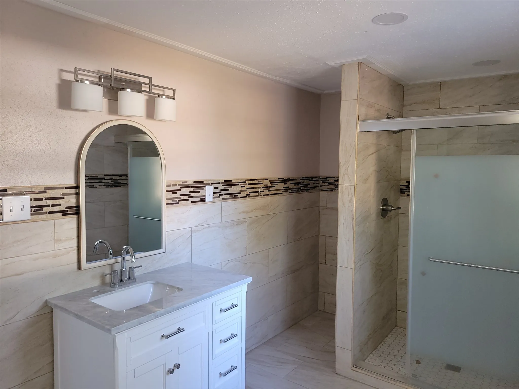 White vanity with a light-toned countertop, chrome fixtures, and an arched mirror