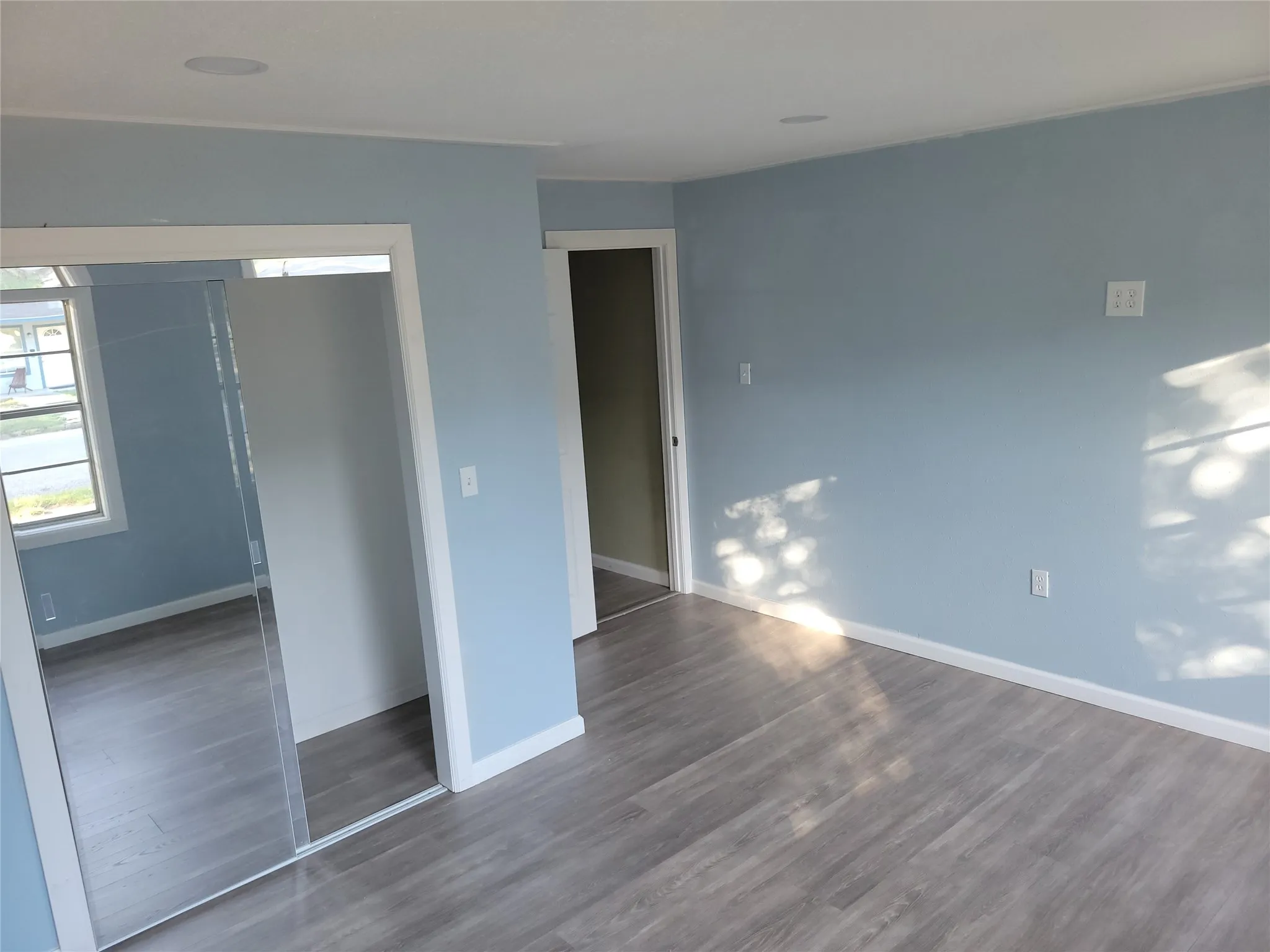 Light blue wall color with white trim, wood-finish flooring, recessed lighting, and mirrored closet doors