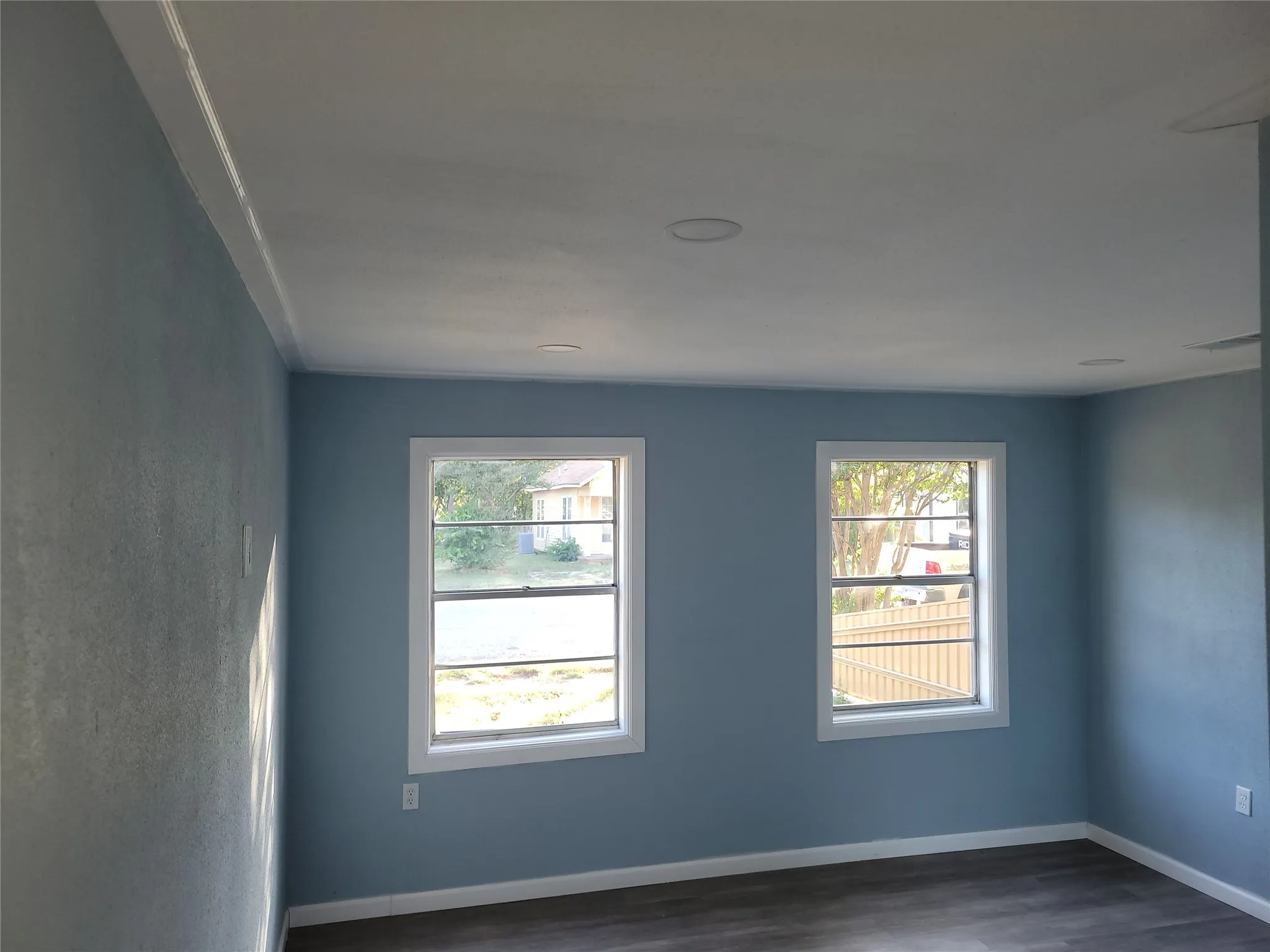 Recessed ceiling lighting, crown molding, two windows with white trim, wood-finish flooring, and light blue wall finish