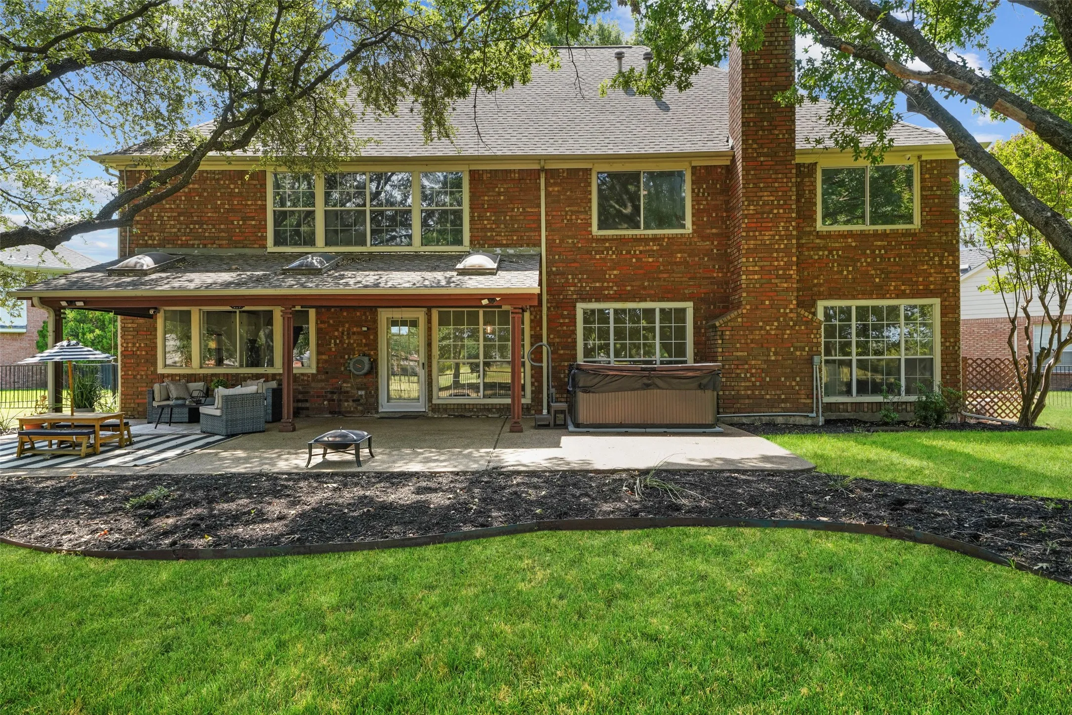 Brick exterior with multiple windows, covered patio, concrete patio, and a hot tub