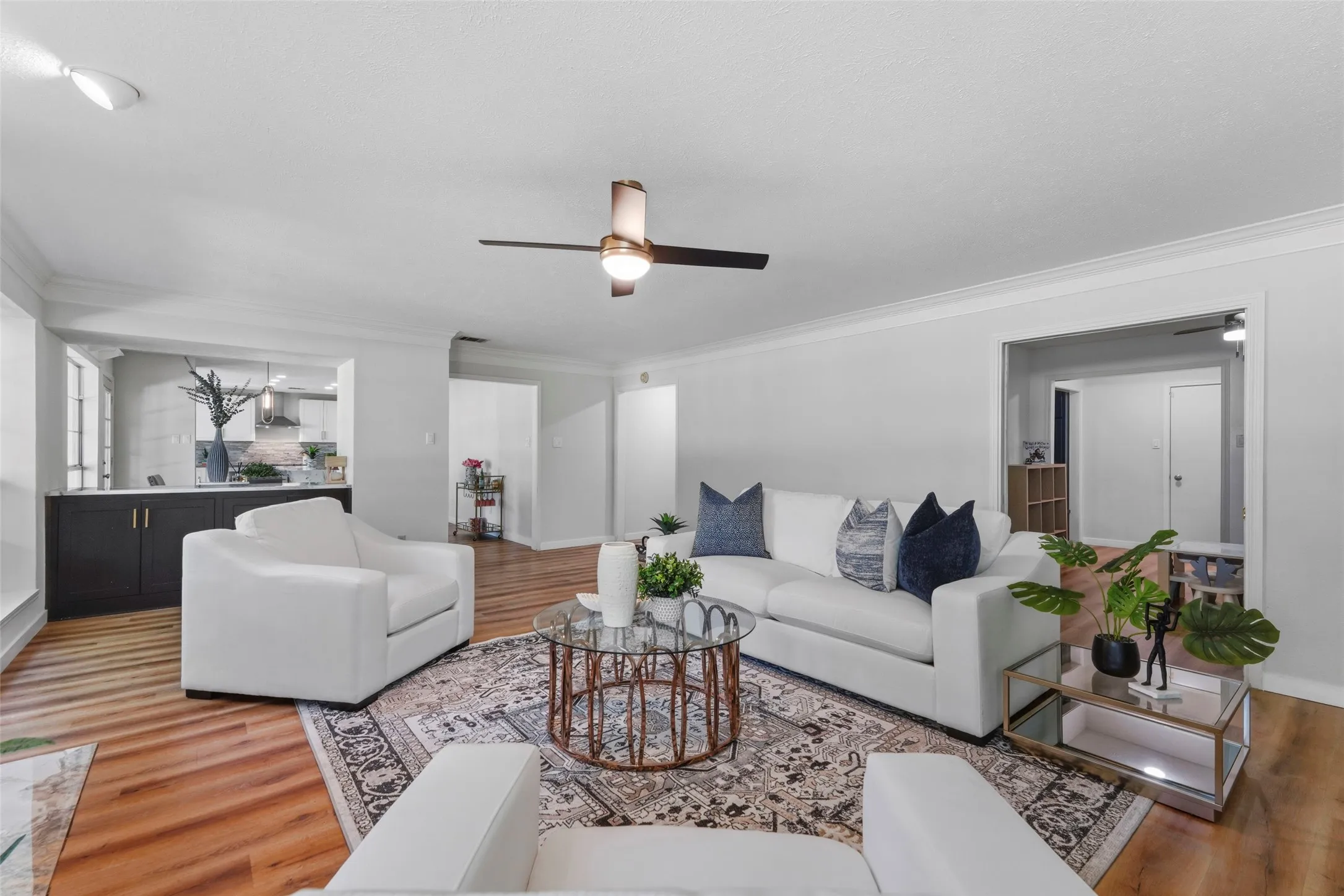 Open-concept living space featuring wood-finish flooring, a ceiling fan, and crown molding
