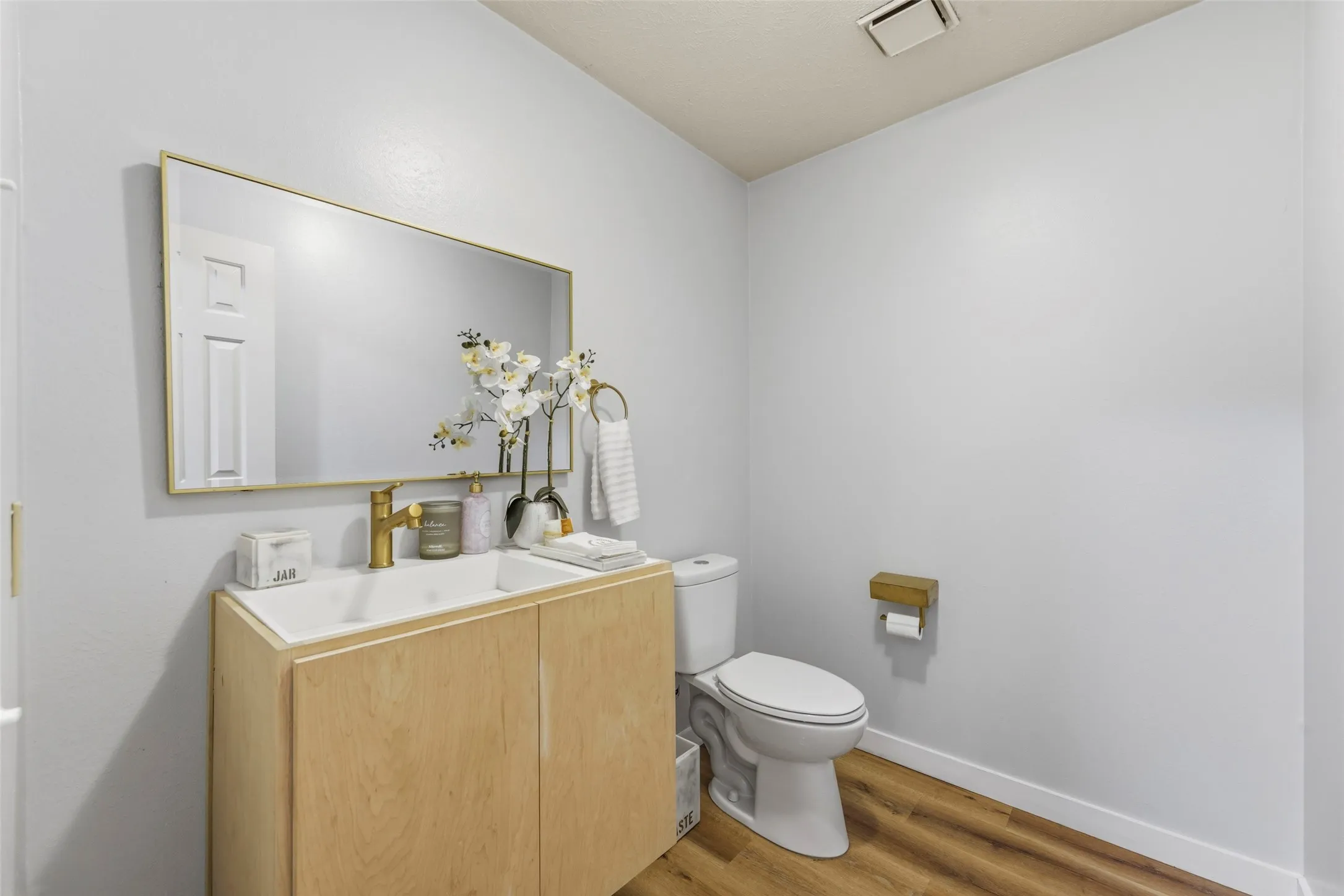 White rectangular sink with a single gold-finish faucet, set into a light wood-finish vanity