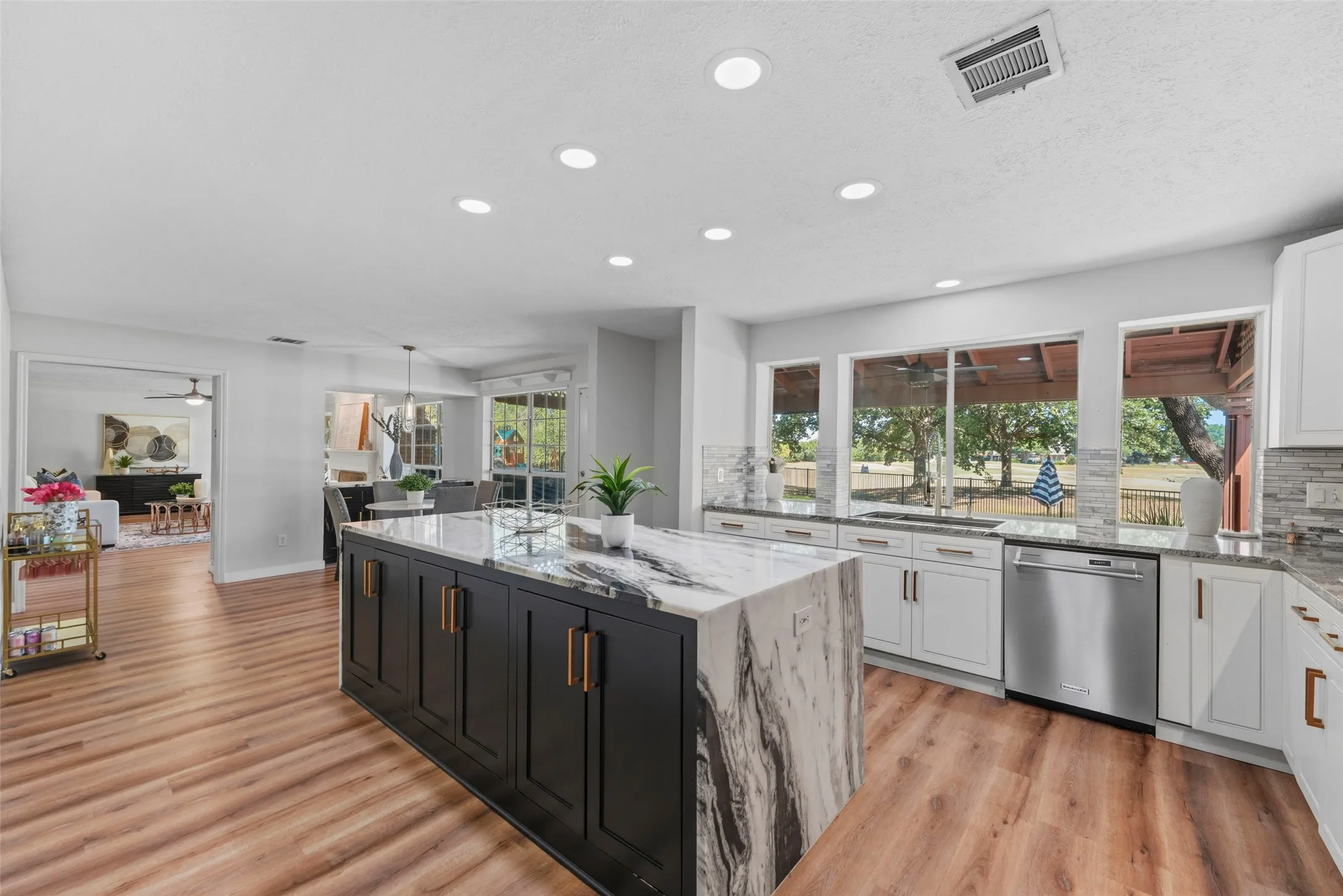Spacious kitchen featuring a large central island with waterfall countertop, white cabinetry, wood-finish flooring, and recessed lighting
