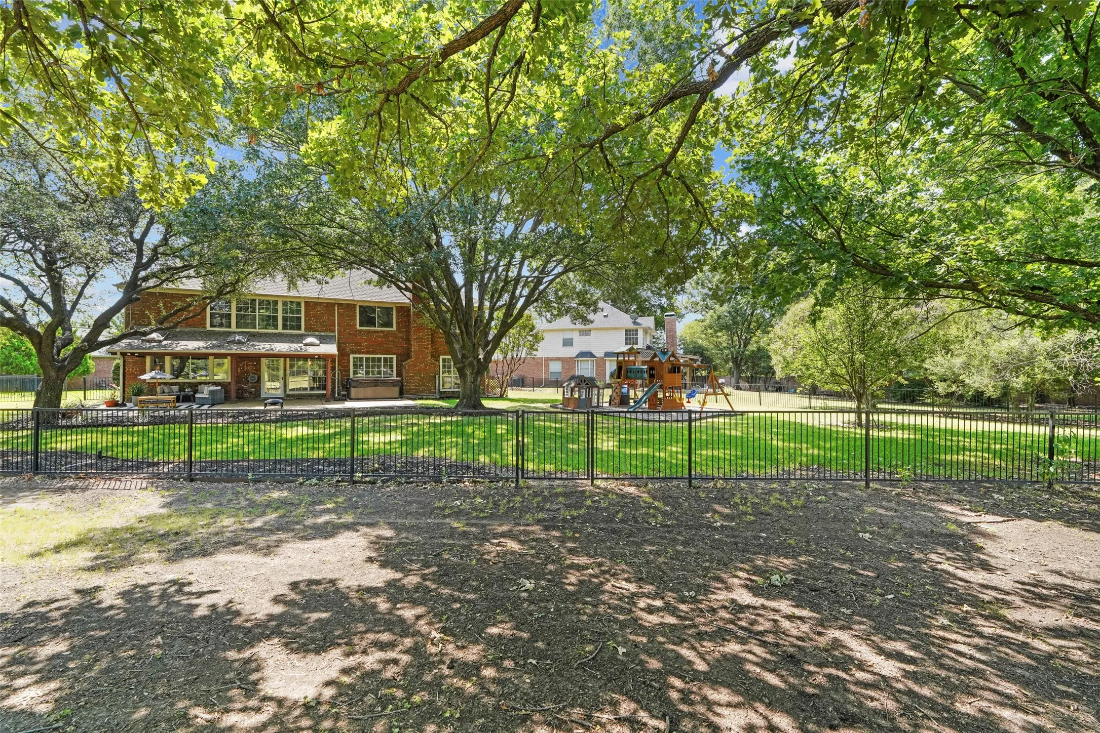 Spacious backyard featuring a dedicated play area with a swingset and slide, established trees, and a brick exterior