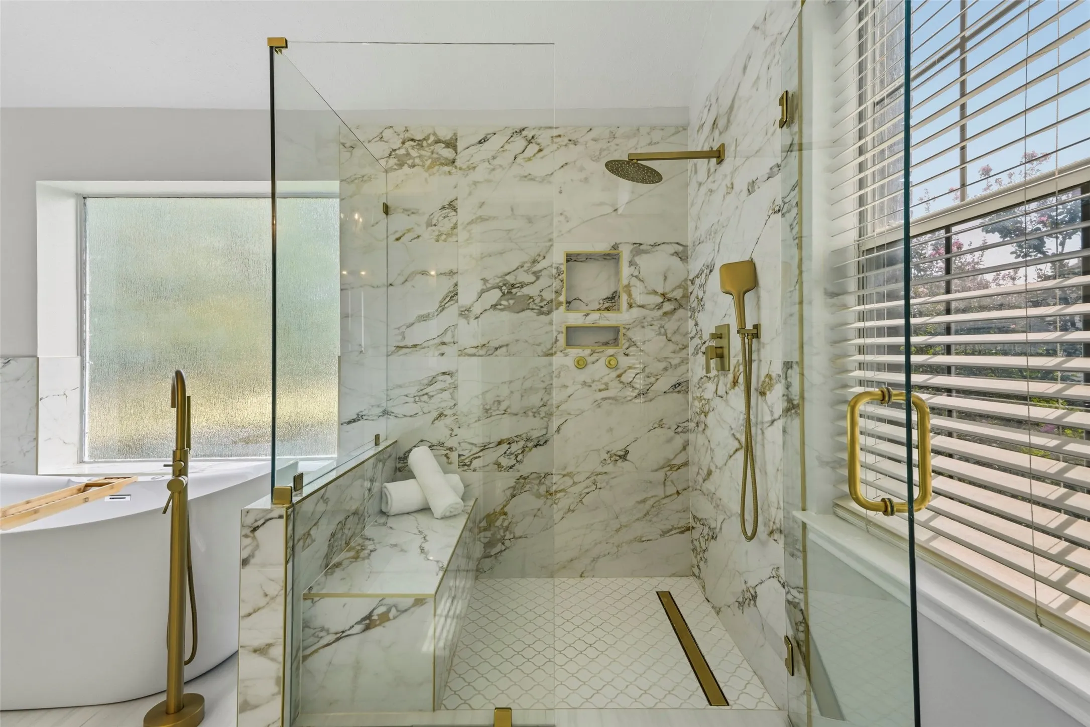 Glass-enclosed shower with marble-patterned walls, built-in shower bench, and gold-finish fixtures