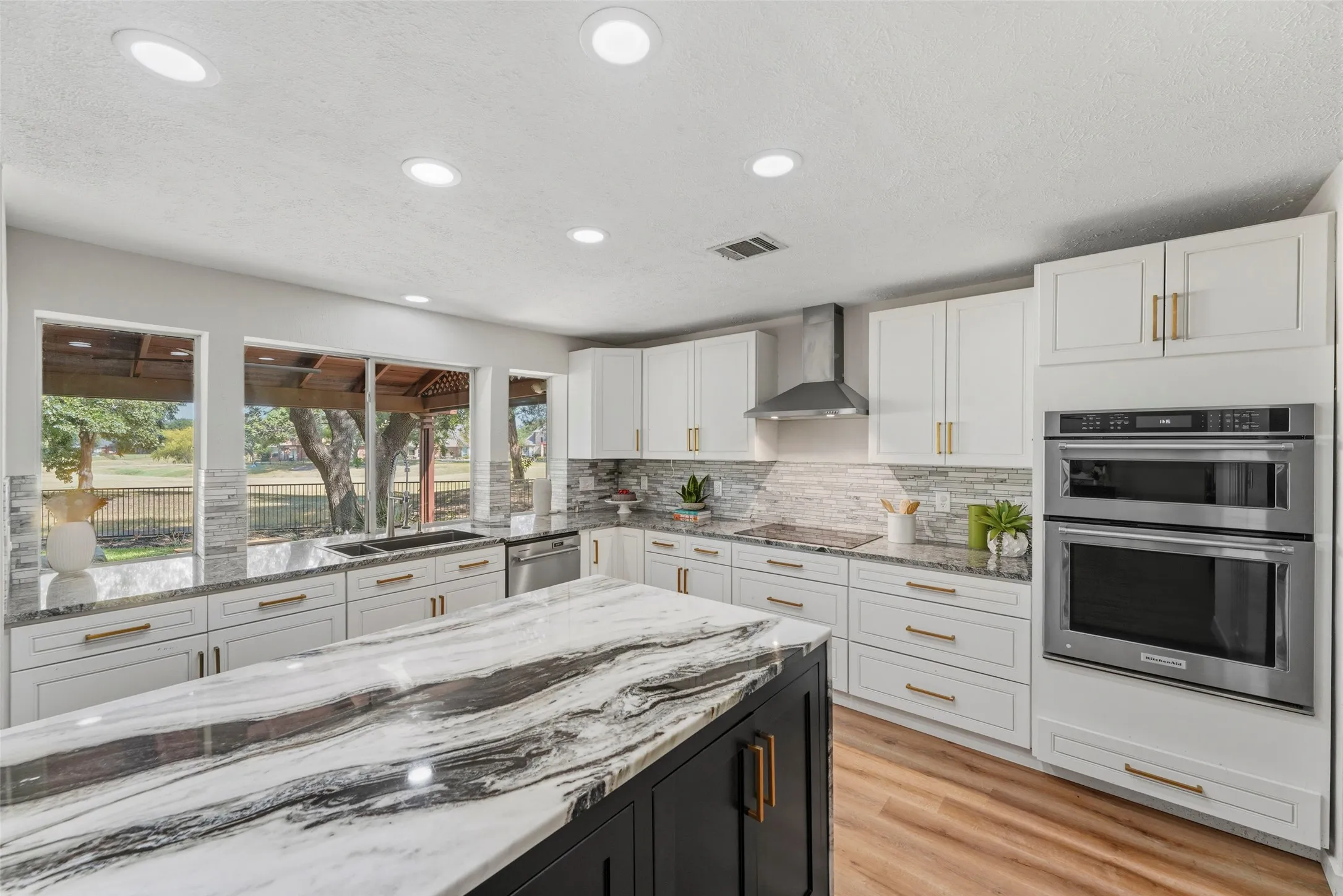 Gourmet kitchen with an expansive island, white cabinetry, dark contrasting island base, stainless steel appliances, and wood-finish flooring