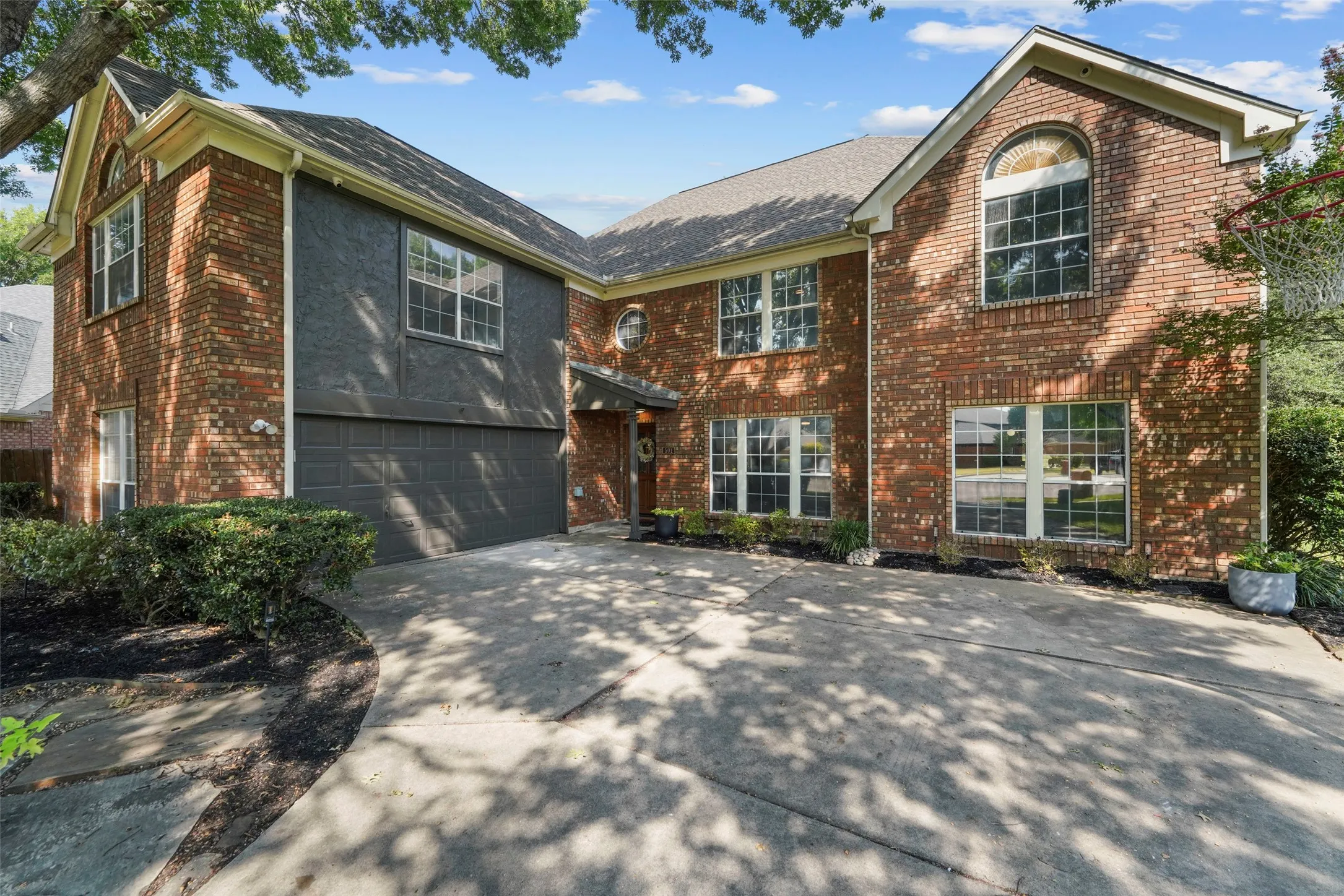 Brick and stucco facade with multiple windows, an arched window, and an attached two-car garage