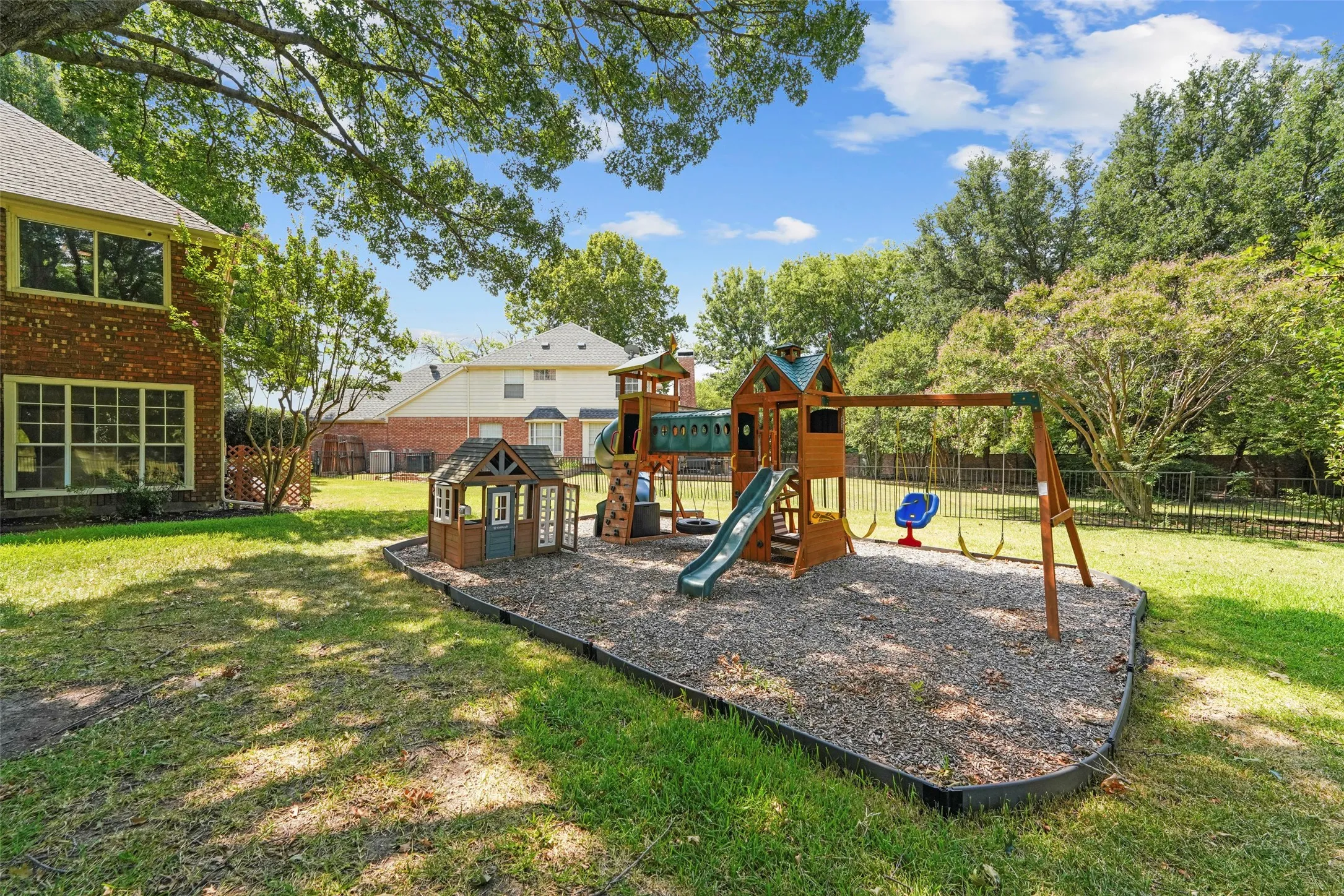 Spacious backyard featuring a dedicated play area with a swingset and slide, established trees, and a brick exterior