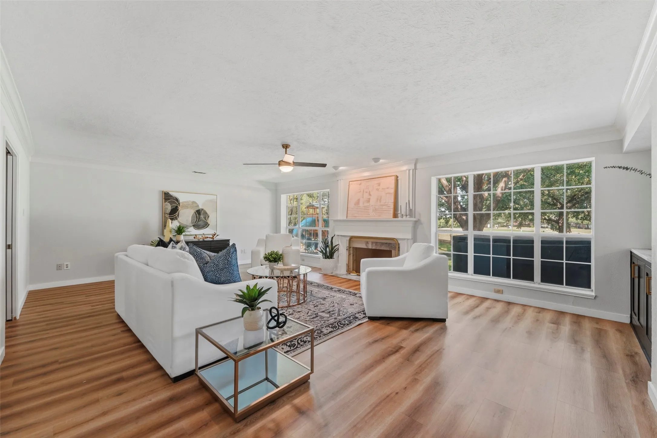 Spacious living area featuring wood-finish flooring, a ceiling fan, crown molding, and large windows