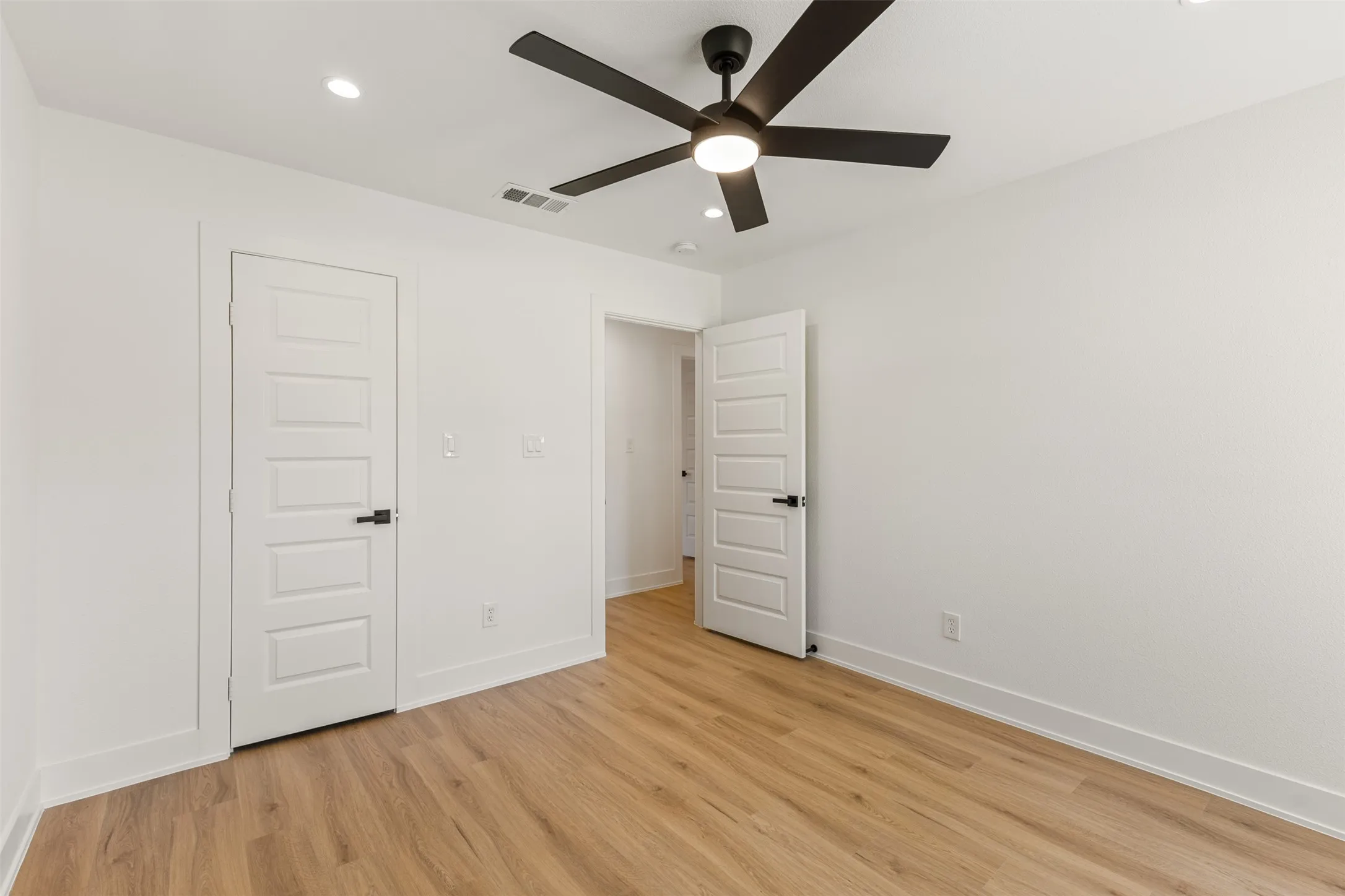 Recessed lighting, wood-finish flooring, white paneled doors with matte black hardware, and a ceiling fan with integrated lighting