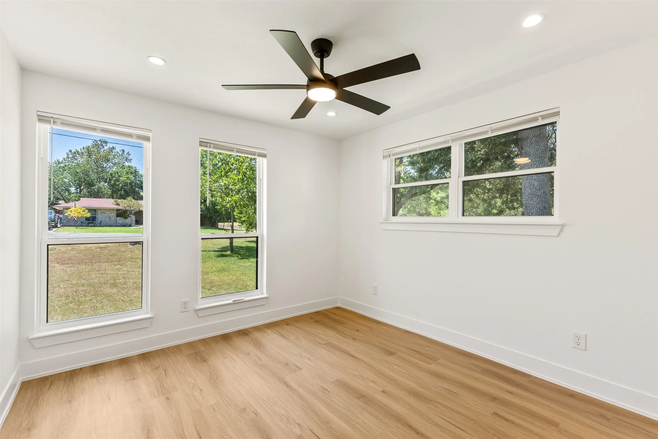 Recessed ceiling lights, a contemporary ceiling fan, wood-finish flooring, and multiple windows
