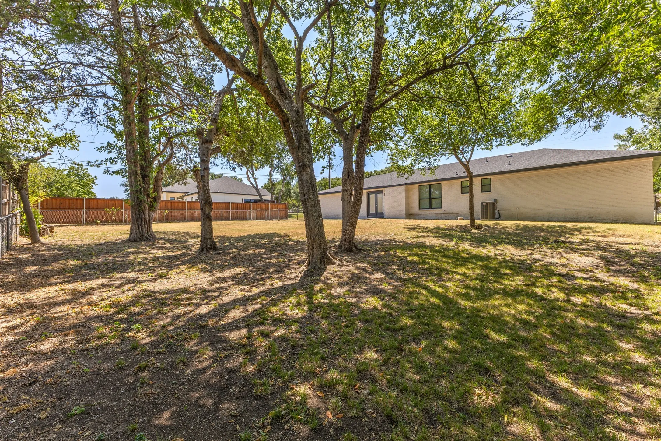 Expansive backyard featuring mature trees, a privacy fence, and a stucco exterior with double doors