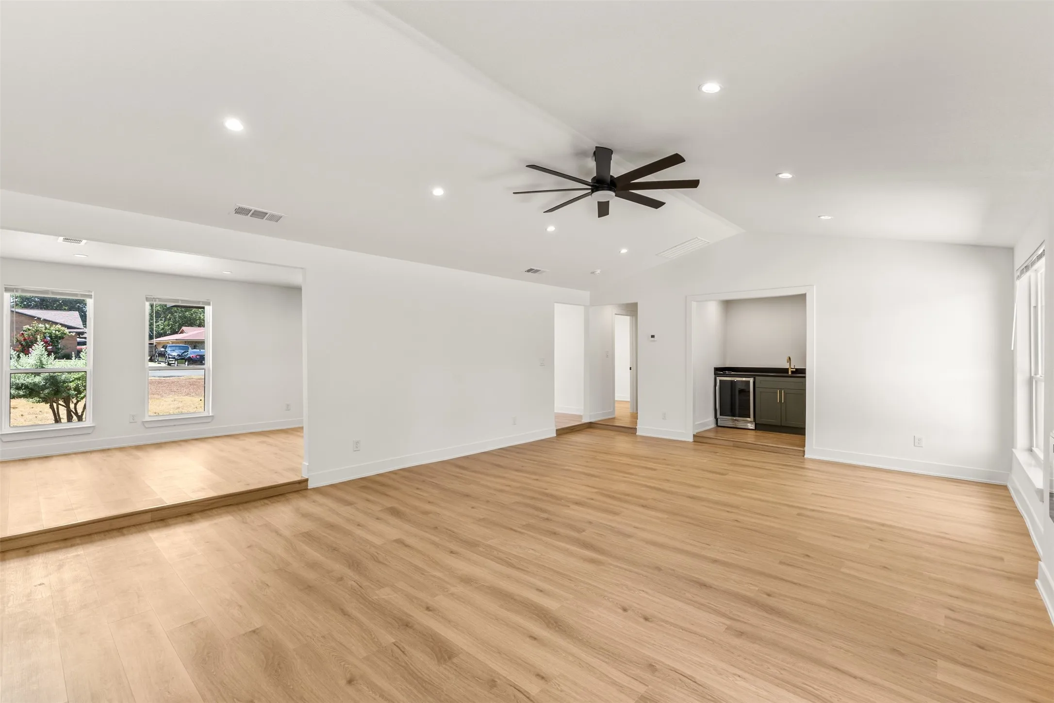Open-concept living area featuring vaulted ceilings, recessed lighting, wood-finish flooring, a built-in wet bar, and a contemporary ceiling fan