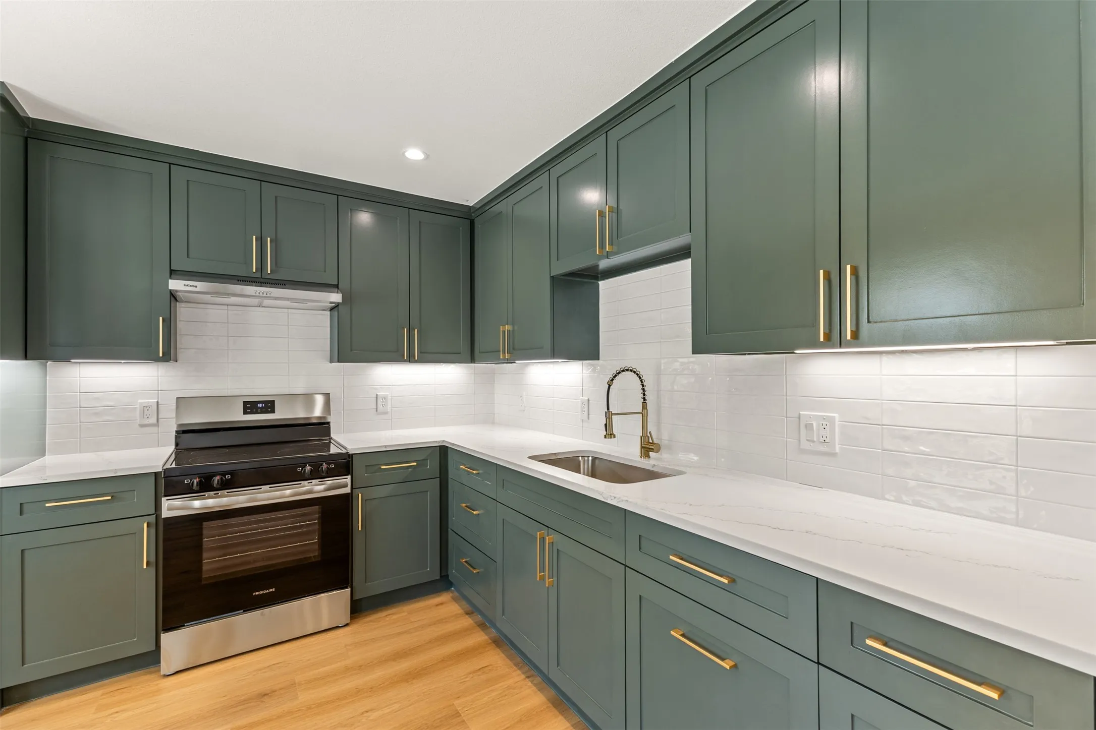 Kitchen with sage cabinetry, gold-tone hardware, stainless steel appliances, white quartz countertops, and wood-finish flooring