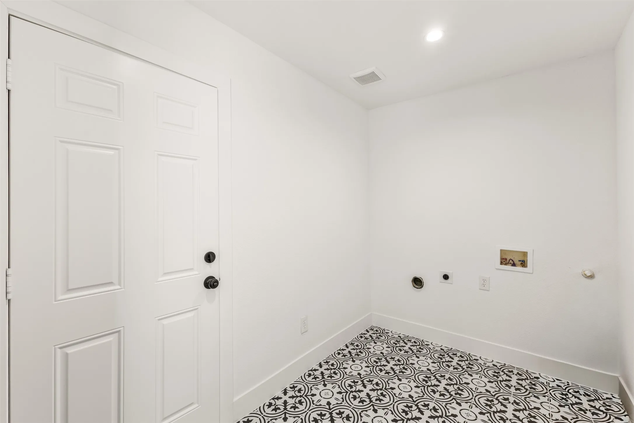 Laundry area featuring patterned floor tiles, recessed lighting, and white paneled door