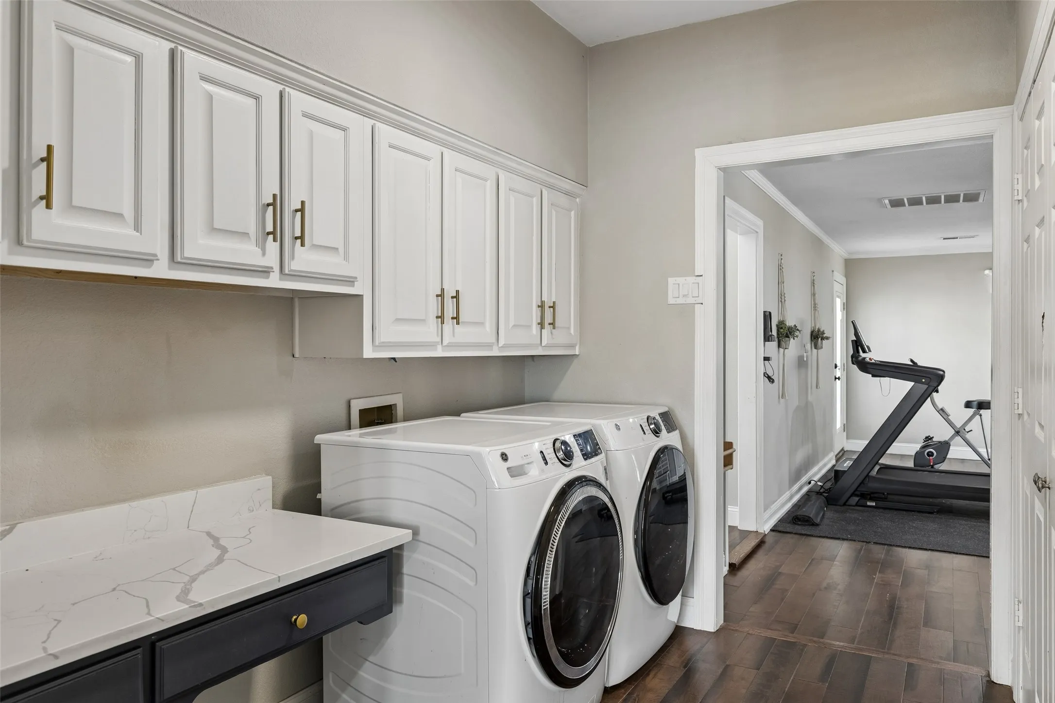 White shaker-style cabinetry with gold-tone hardware, a white countertop with gray veining, and wood-finish flooring