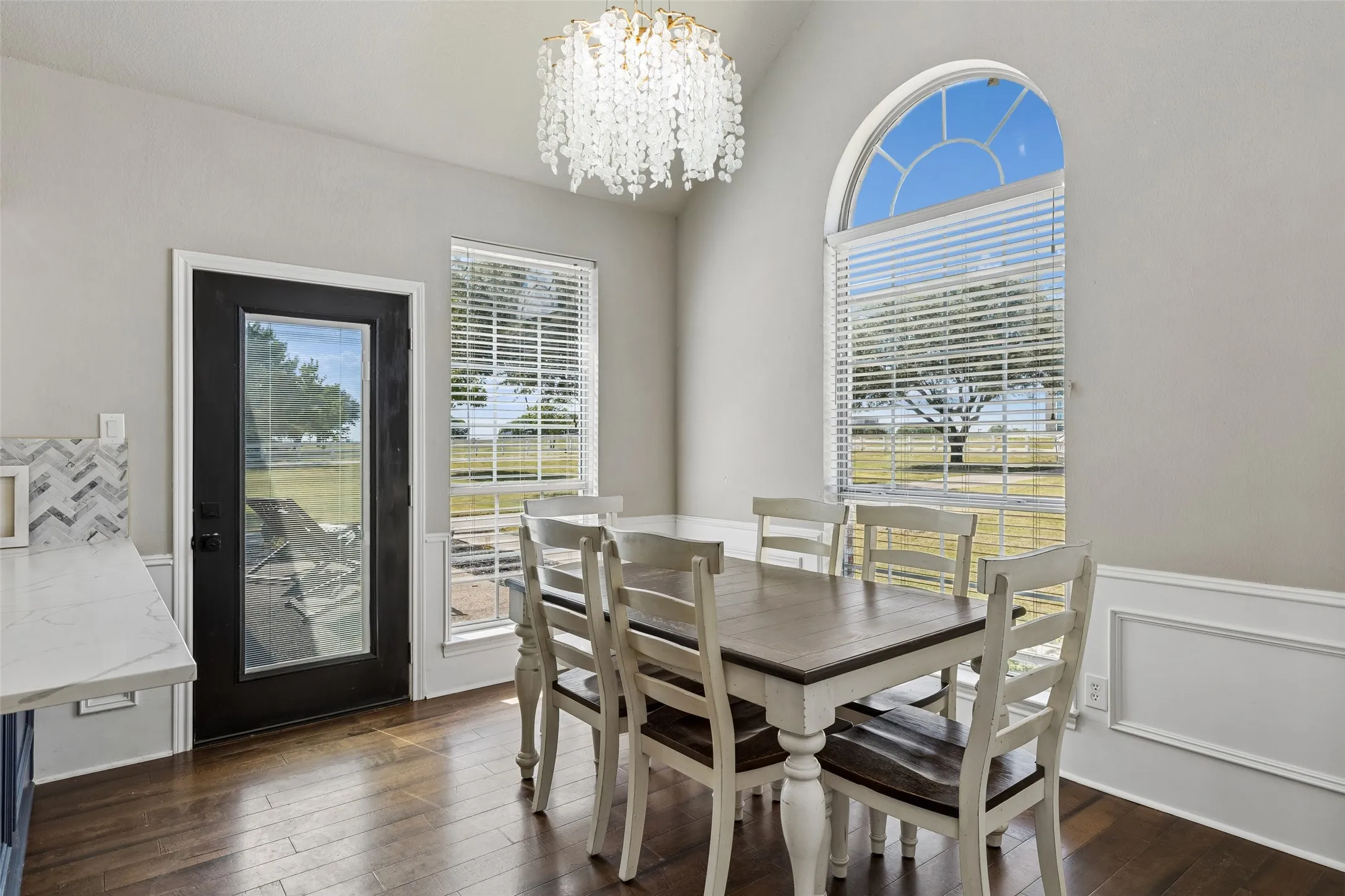 Vaulted ceiling featuring a crystal chandelier, wood-finish flooring, and wainscoting