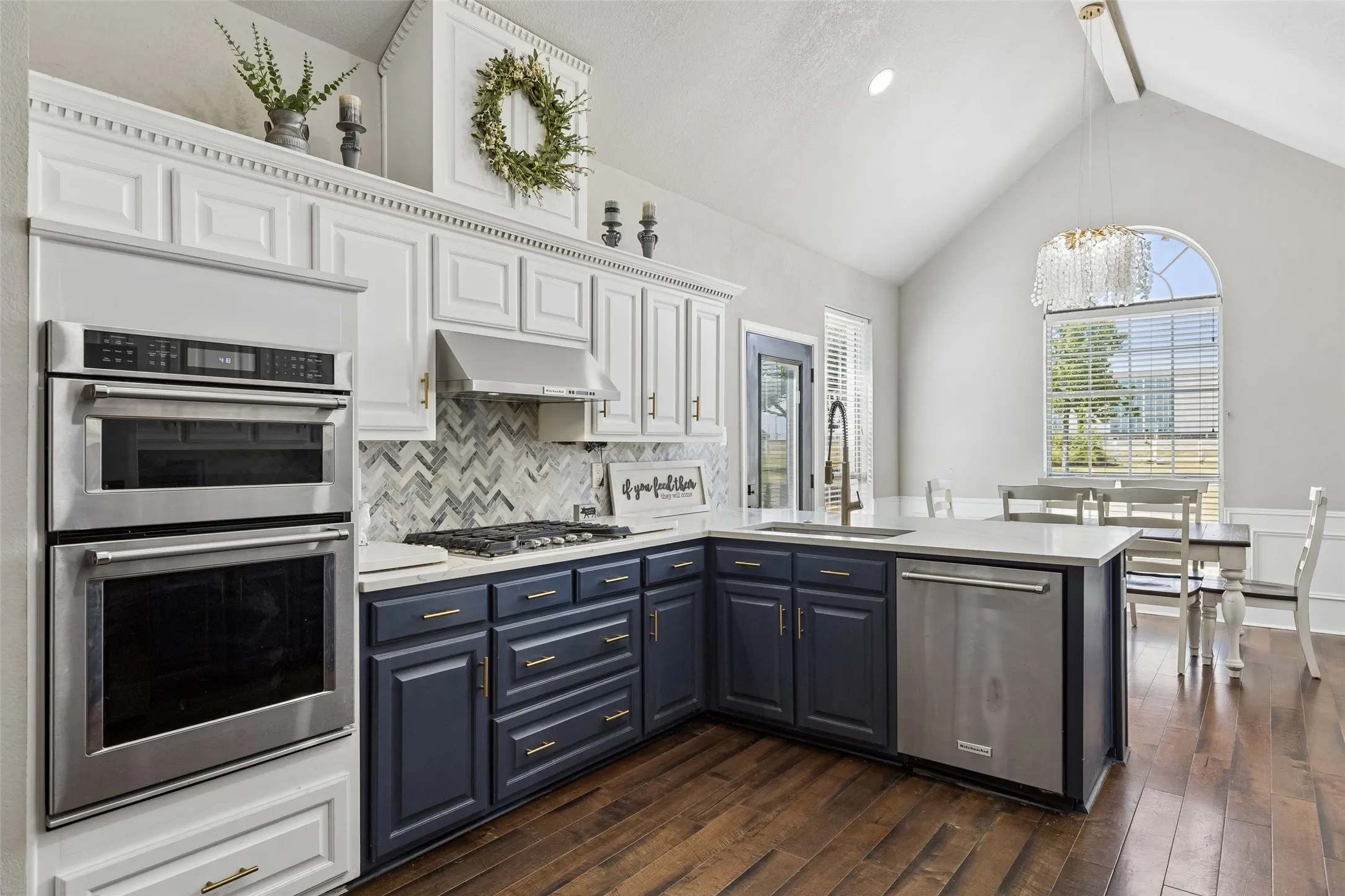 Vaulted ceiling, wood-finish flooring, stainless steel appliances, kitchen island with sink, and a herringbone tile backsplash