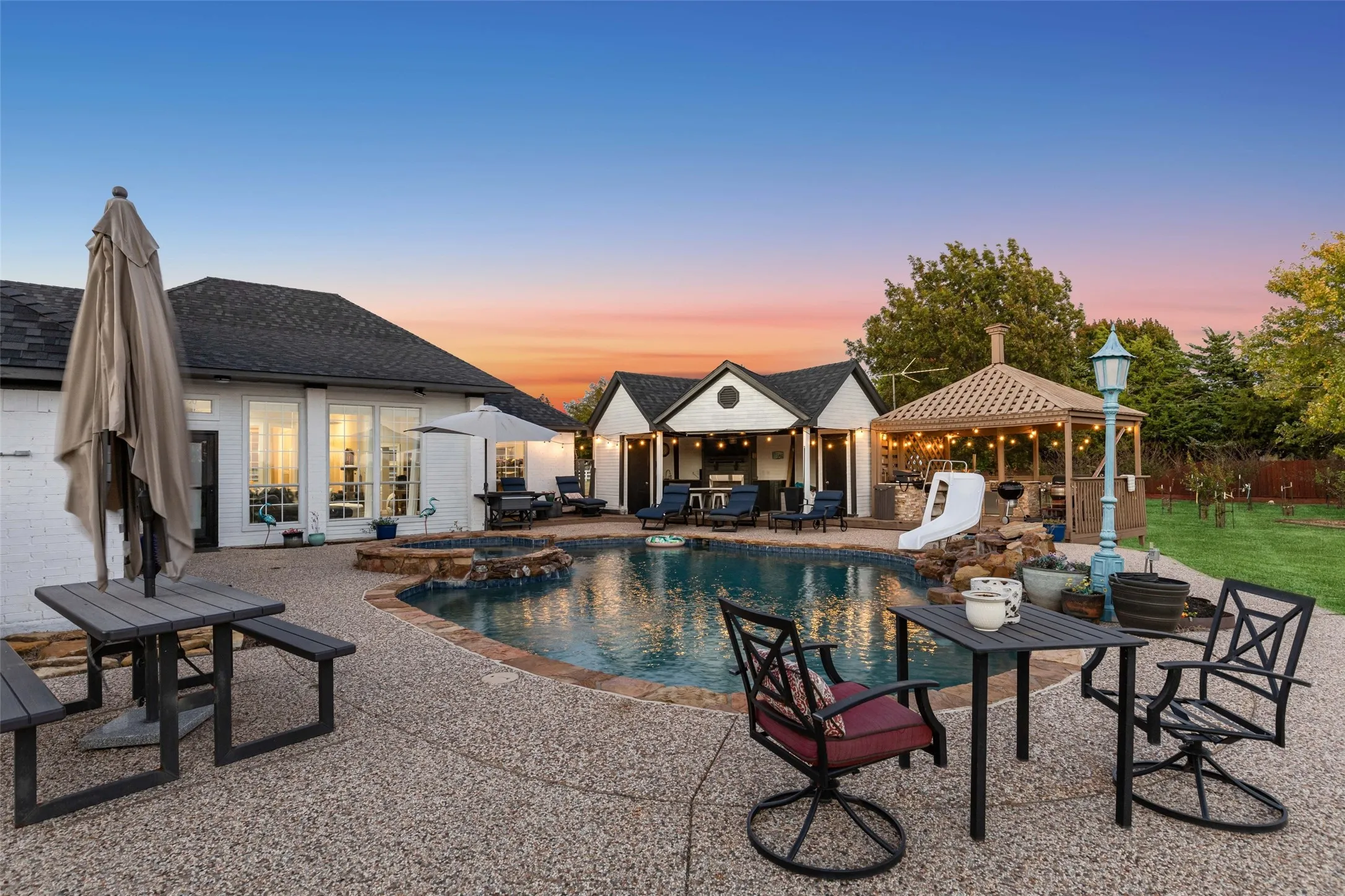 Expansive backyard featuring a free-form swimming pool with a stone coping, a built-in fire pit, a covered outdoor kitchen, and a separate gazebo