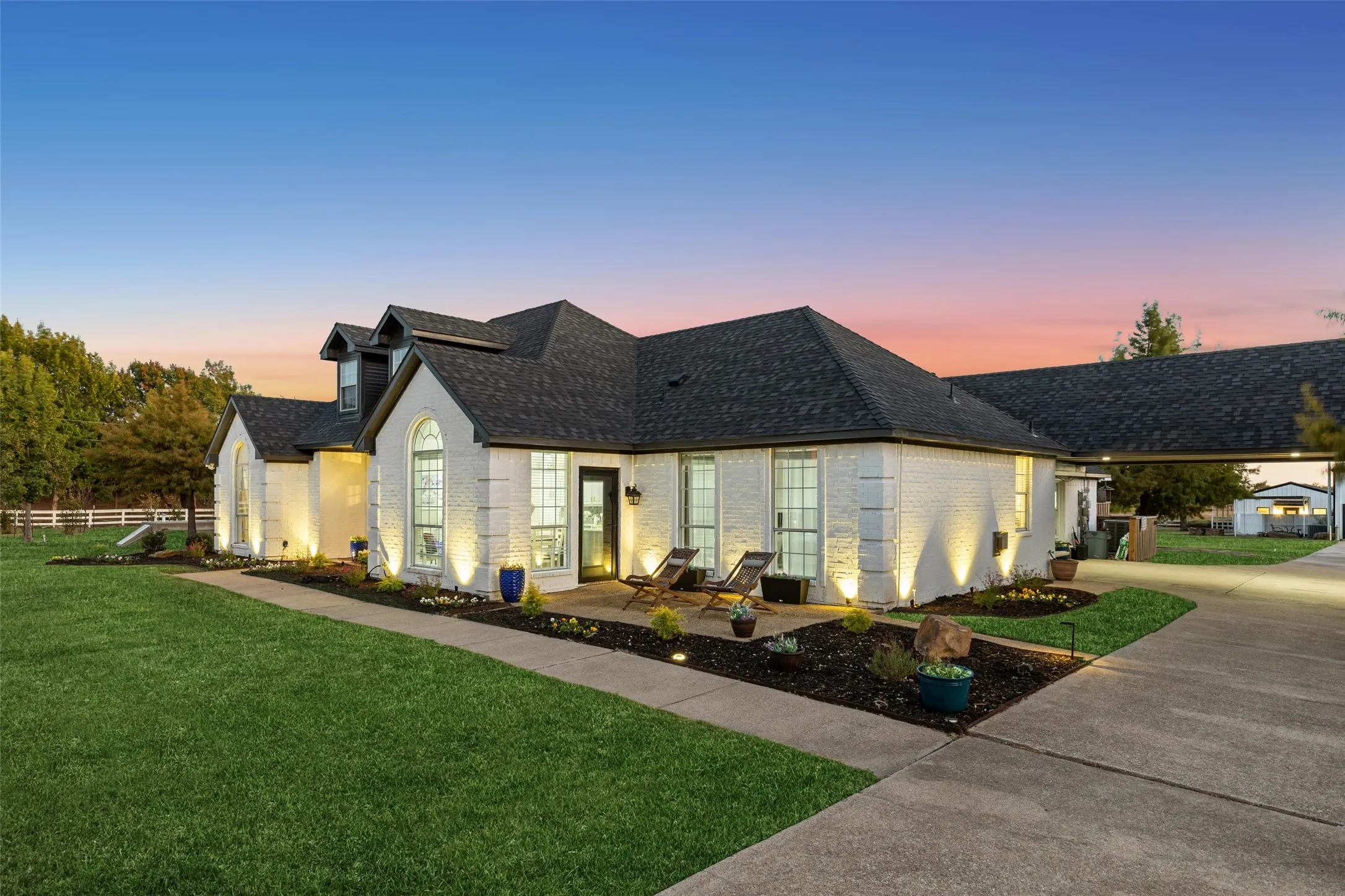 White brick exterior with dark shingle roofing, concrete driveway, and established landscaping