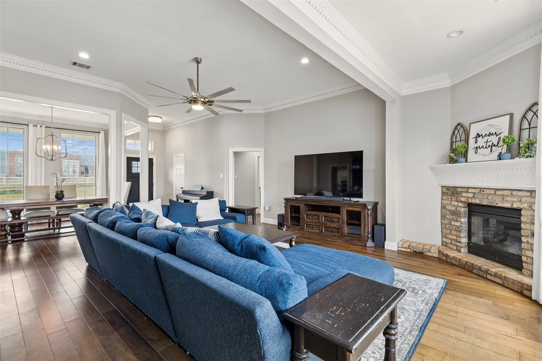 Hardwood flooring, crown molding, brick fireplace with mantel, ceiling fan, and recessed lighting