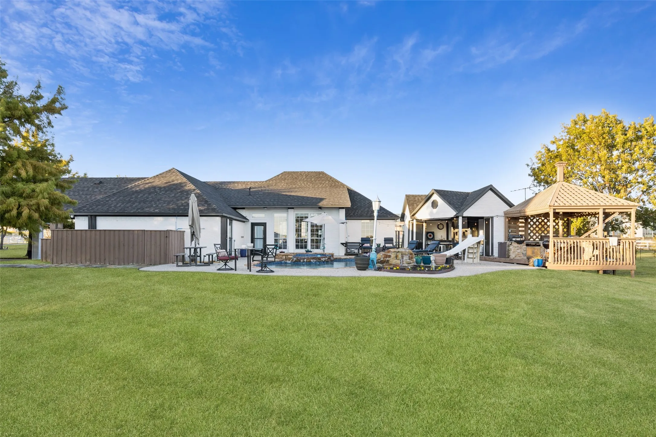 Expansive backyard featuring a manicured lawn, a large concrete patio, and a wooden gazebo