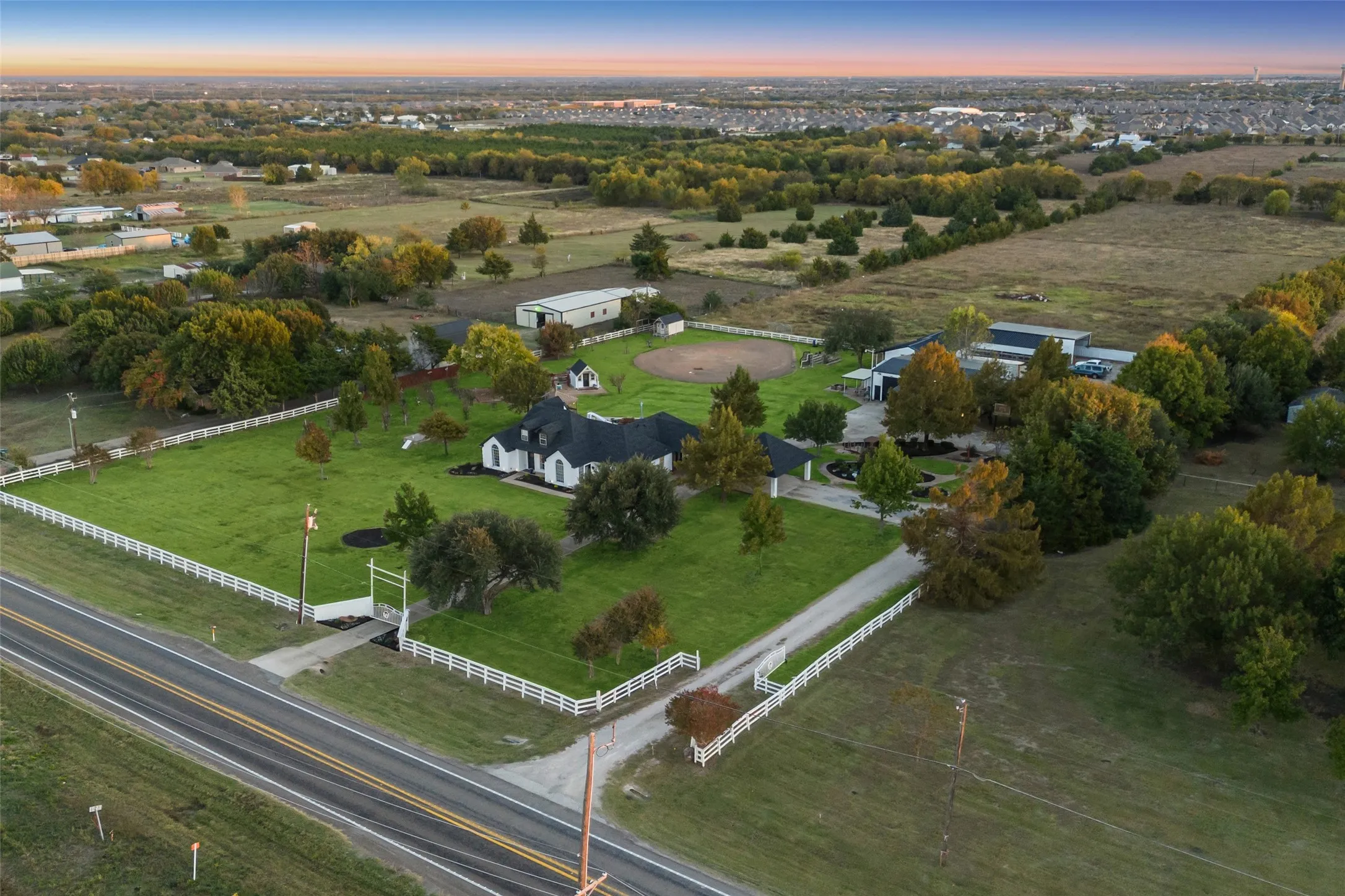 Expansive property featuring a white fence perimeter, a main residence with a dark roof, a baseball diamond, and outbuildings
