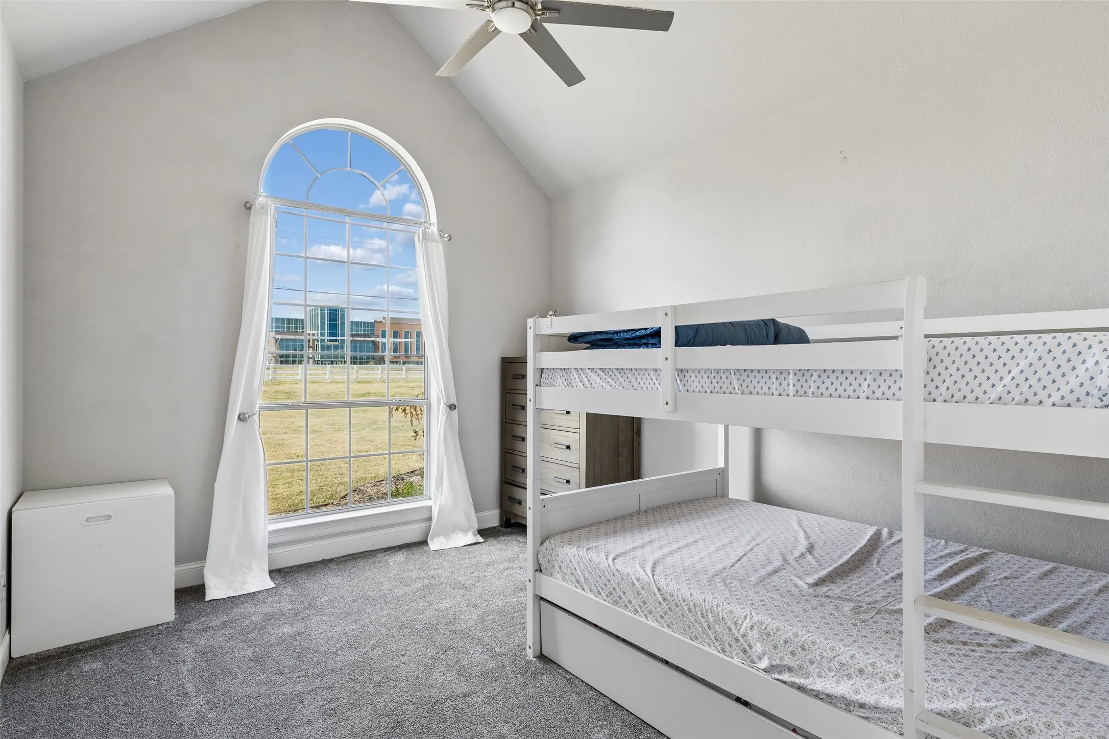 Arched window with gridded panes, high vaulted ceiling, ceiling fan, and grey carpeting