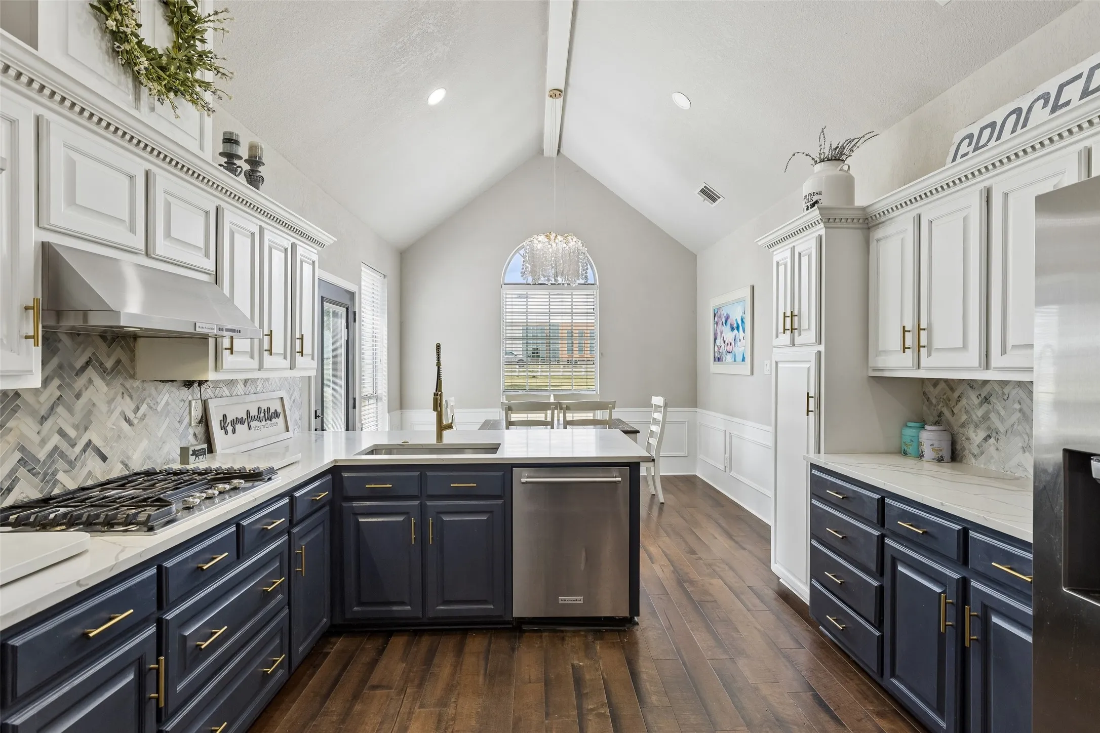 Vaulted ceiling kitchen featuring two-tone cabinetry, herringbone tile backsplash, stainless steel appliances, and a central island with an undermount​​‌​​​​‌​​‌‌​‌‌​​​‌‌​‌​‌​‌​​​‌​​ sink
