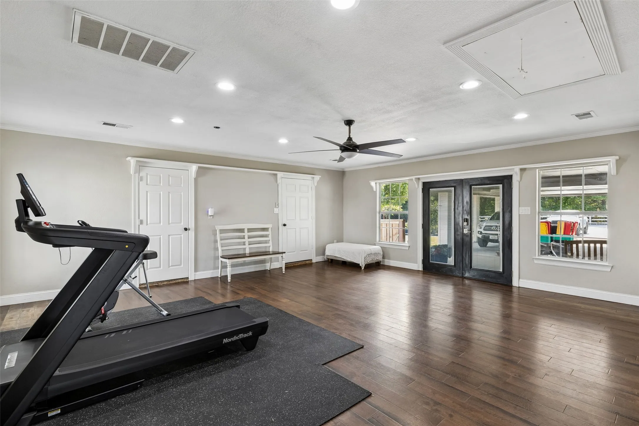 Spacious room featuring wood-finish flooring, two sets of white double doors, two windows, and a ceiling fan with integrated lighting