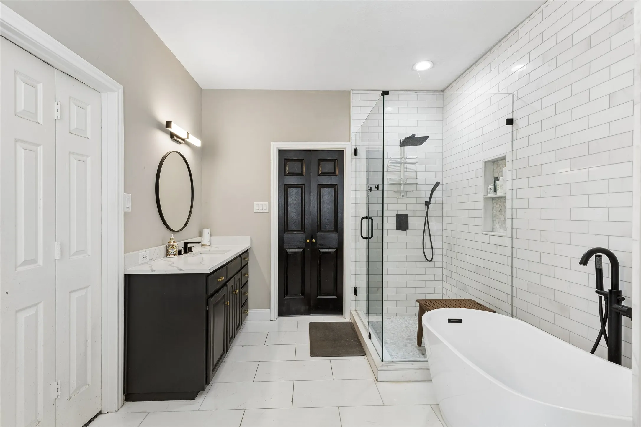 Freestanding soaking tub, walk-in shower with subway tile surround, double vanity with stone countertop, and large format floor tiling
