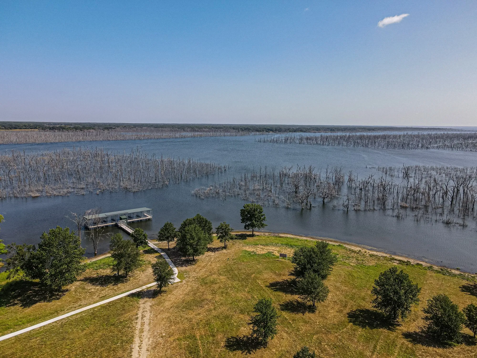 Expansive waterfront property featuring a private boat dock, concrete pathway, and mature trees along the shore