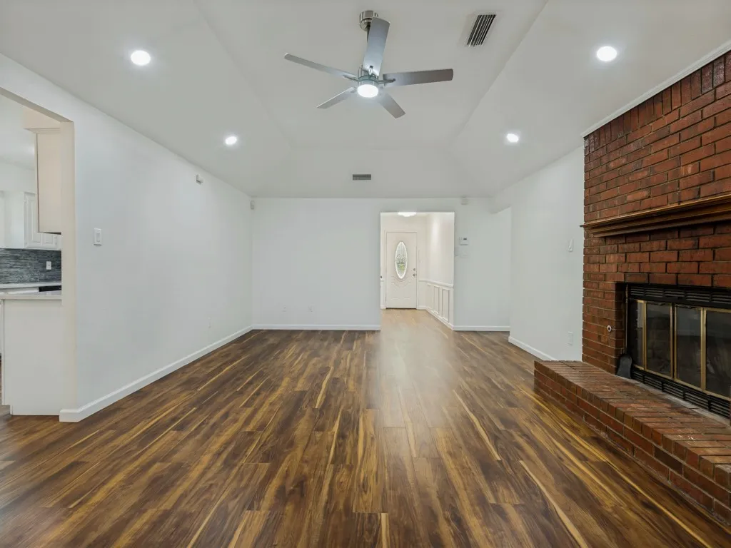 Vaulted ceiling with a ceiling fan and recessed lighting, wood-finish flooring, brick fireplace, and wainscoting